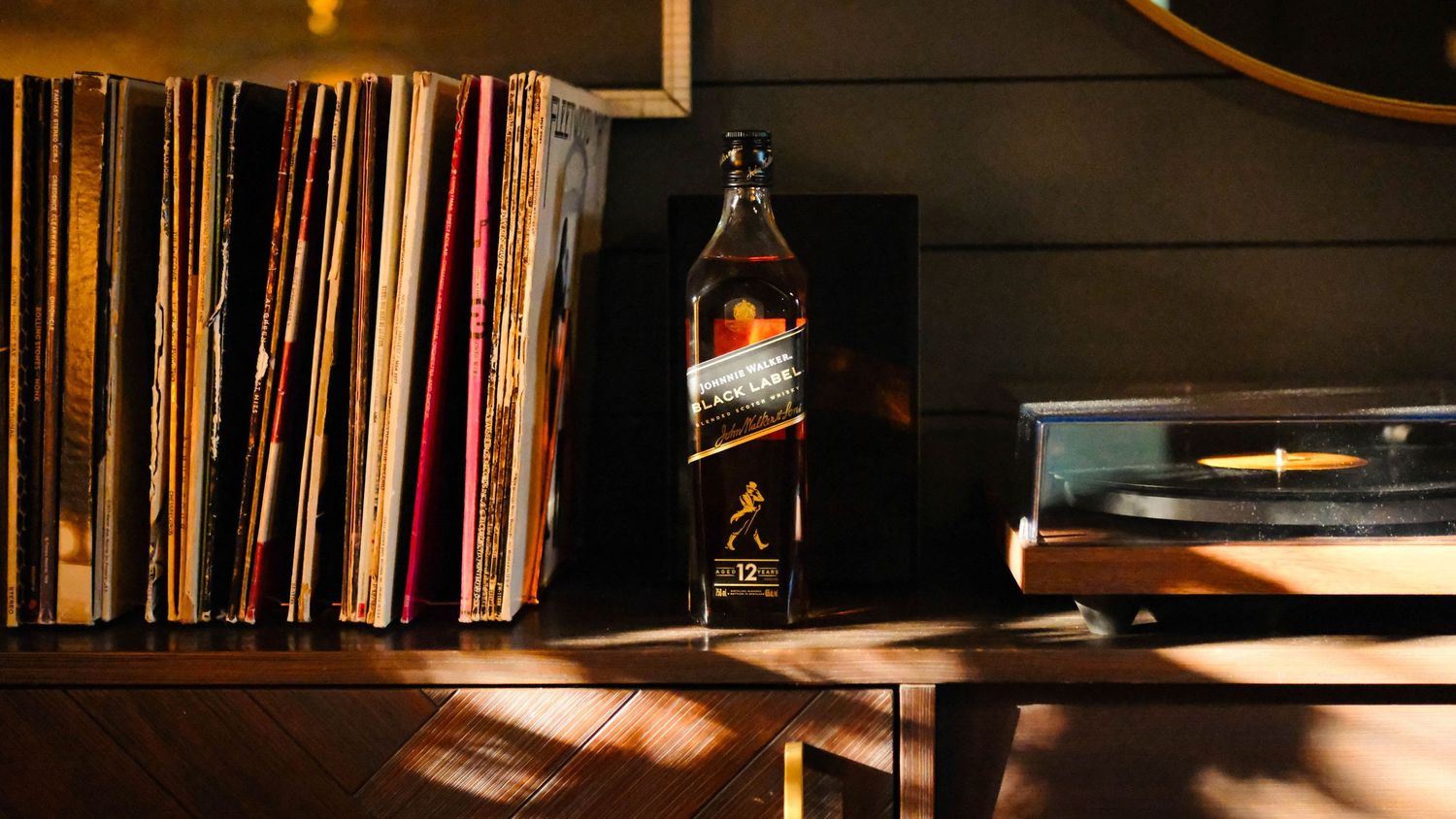 Johnnie Walker bottle displayed beside vinyl records in afternoon light.