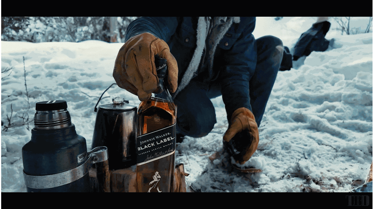 Dog beside a Johnnie Walker bottle and outdoor drinkware in the snow.