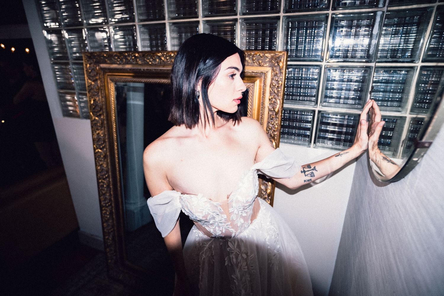 Model in a white gown posing beside an ornate mirror.