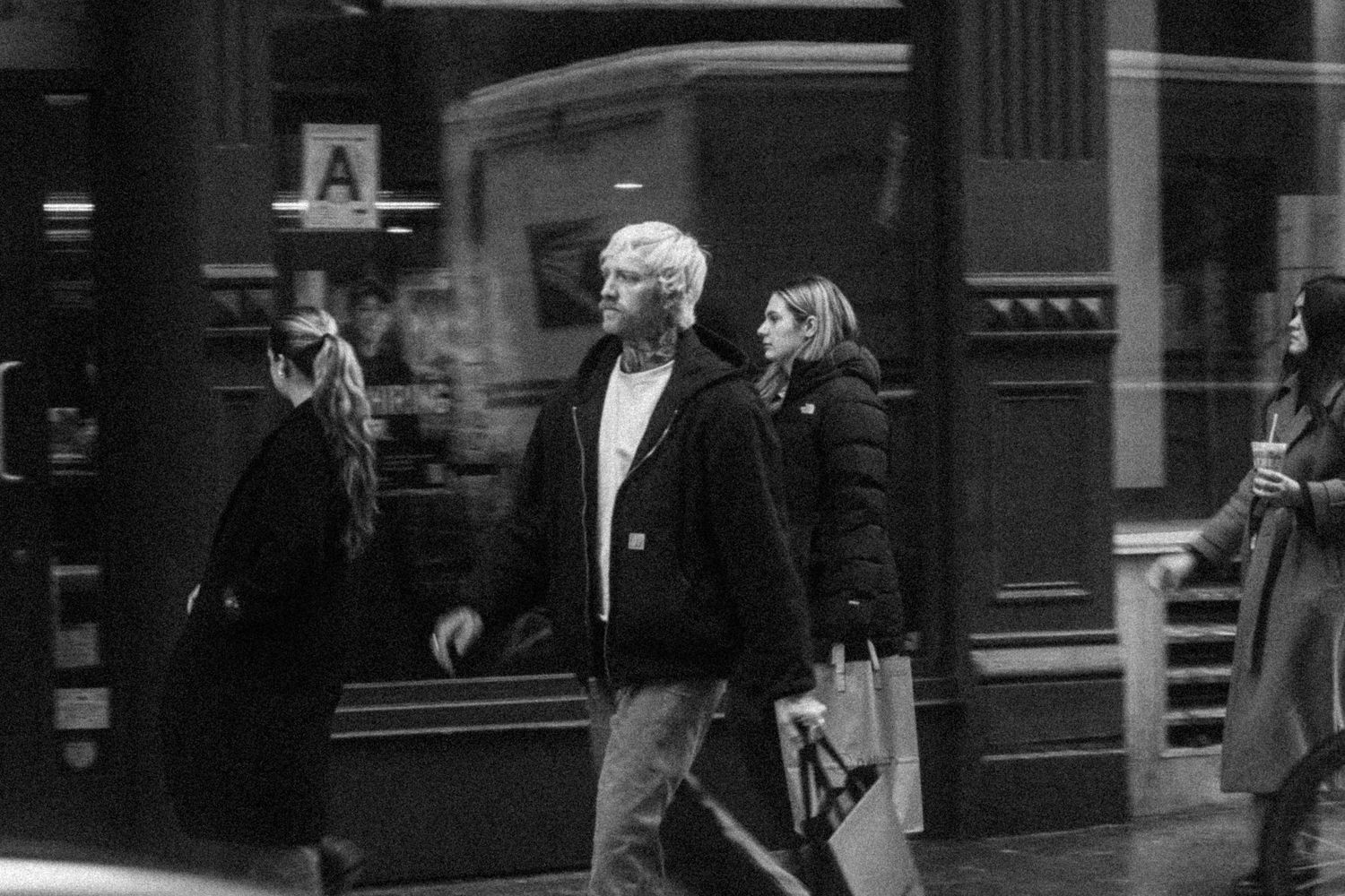Black-and-white NYC street photograph of three pedestrians walking past a storefront.