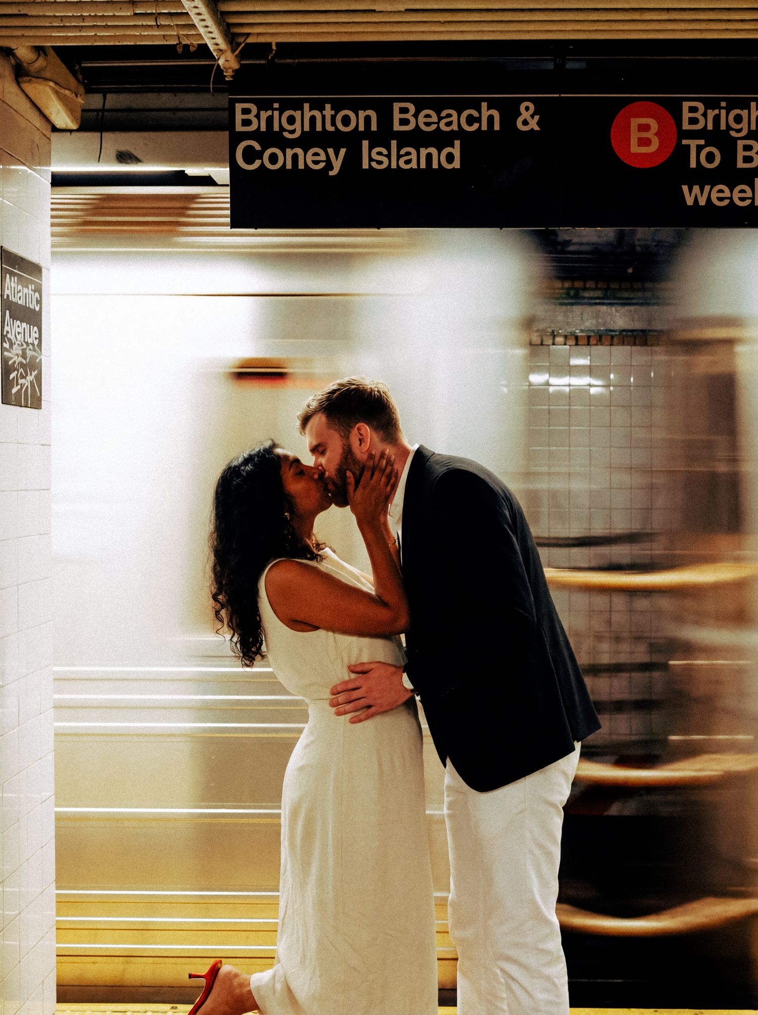 Newlyweds kissing on a subway platform as a New York train passes behind them.