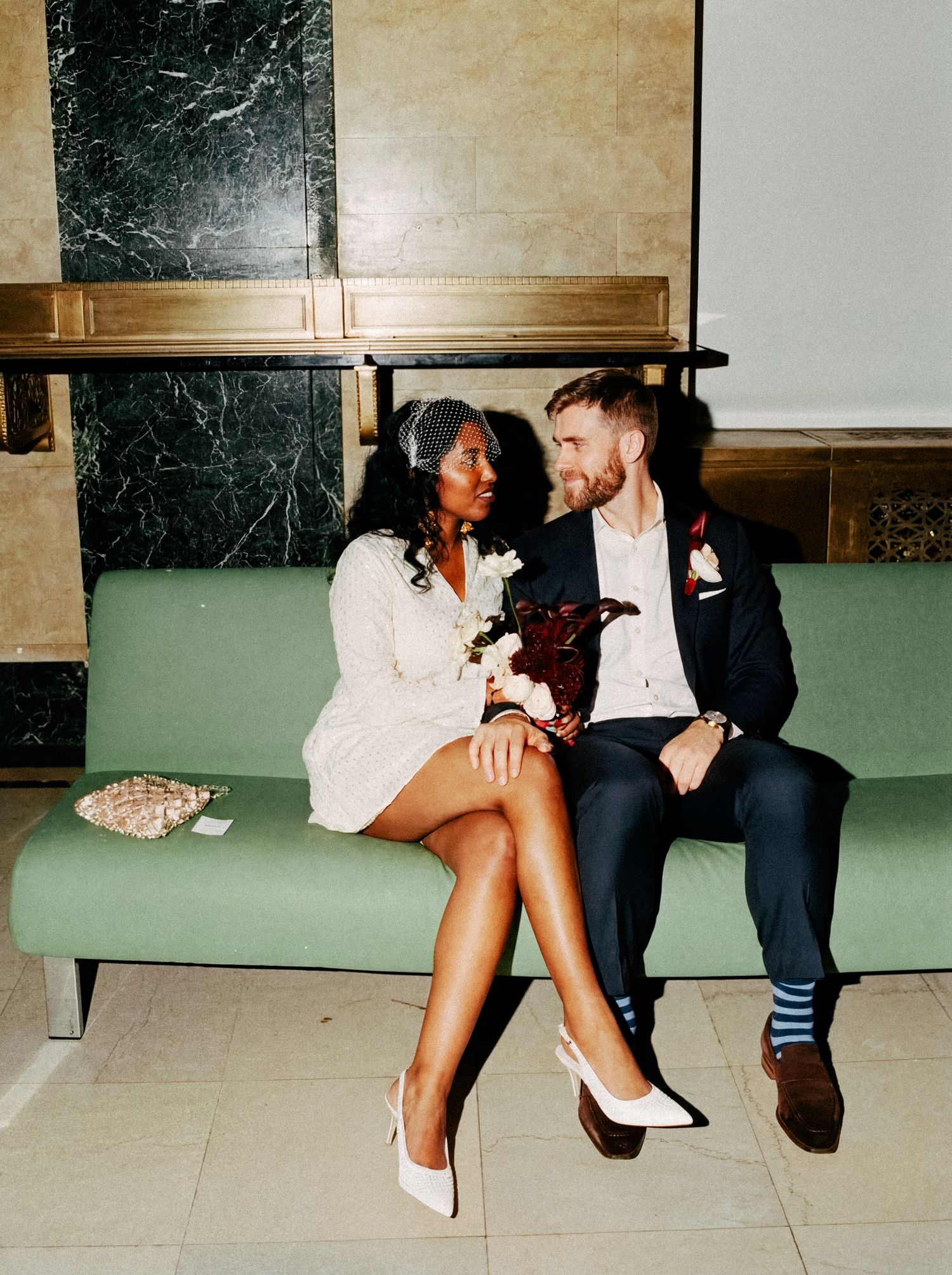 Newlyweds sitting together on a green lounge after their courthouse ceremony.