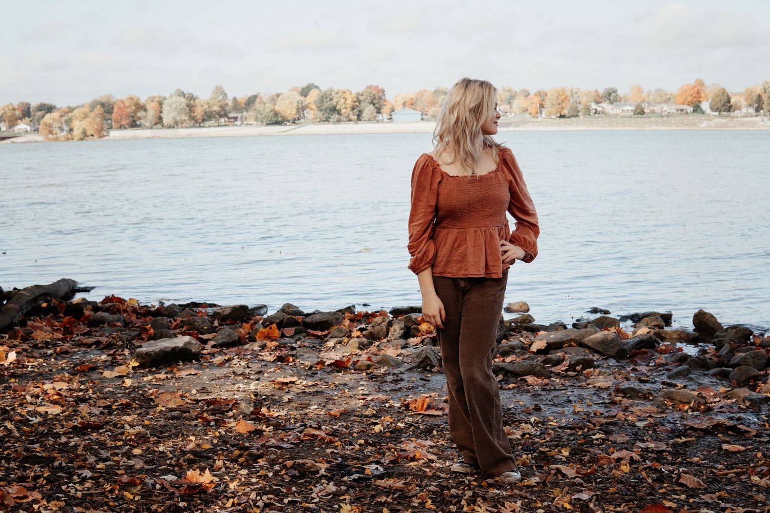 A peaceful scene of someone walking along a rocky shoreline beside a calm lake at sunset.