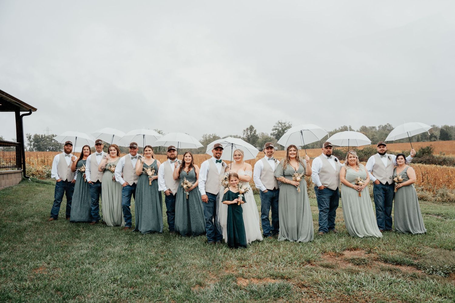 Wedding party in dusty blue gowns and white attire poses together on a rustic outdoor field at sunset.