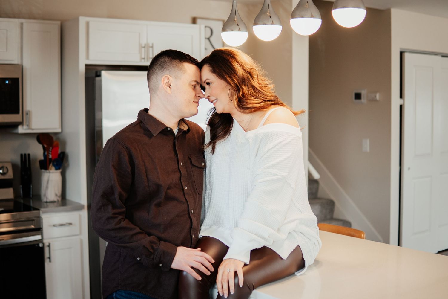 Romantic couple embracing in modern kitchen with pendant lighting.