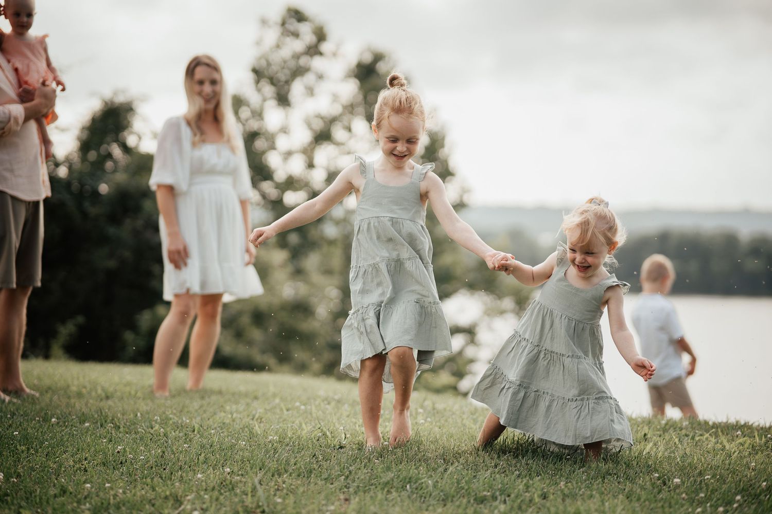 Children playing together on a grassy hillside overlooking a lake on a cloudy day.