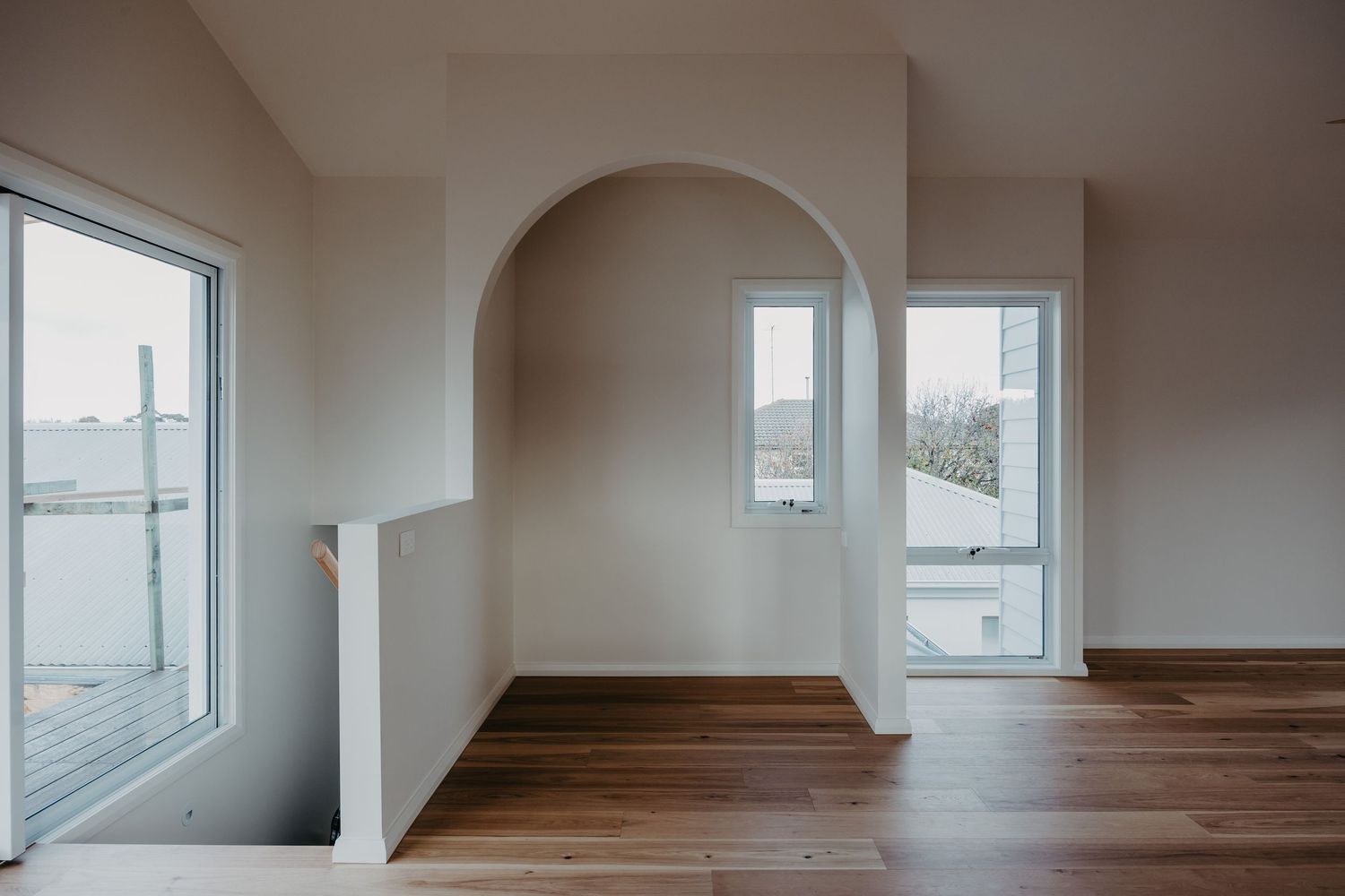 Bright open room with dark timber floors, white walls, arched niche, and multiple windows offering natural light.