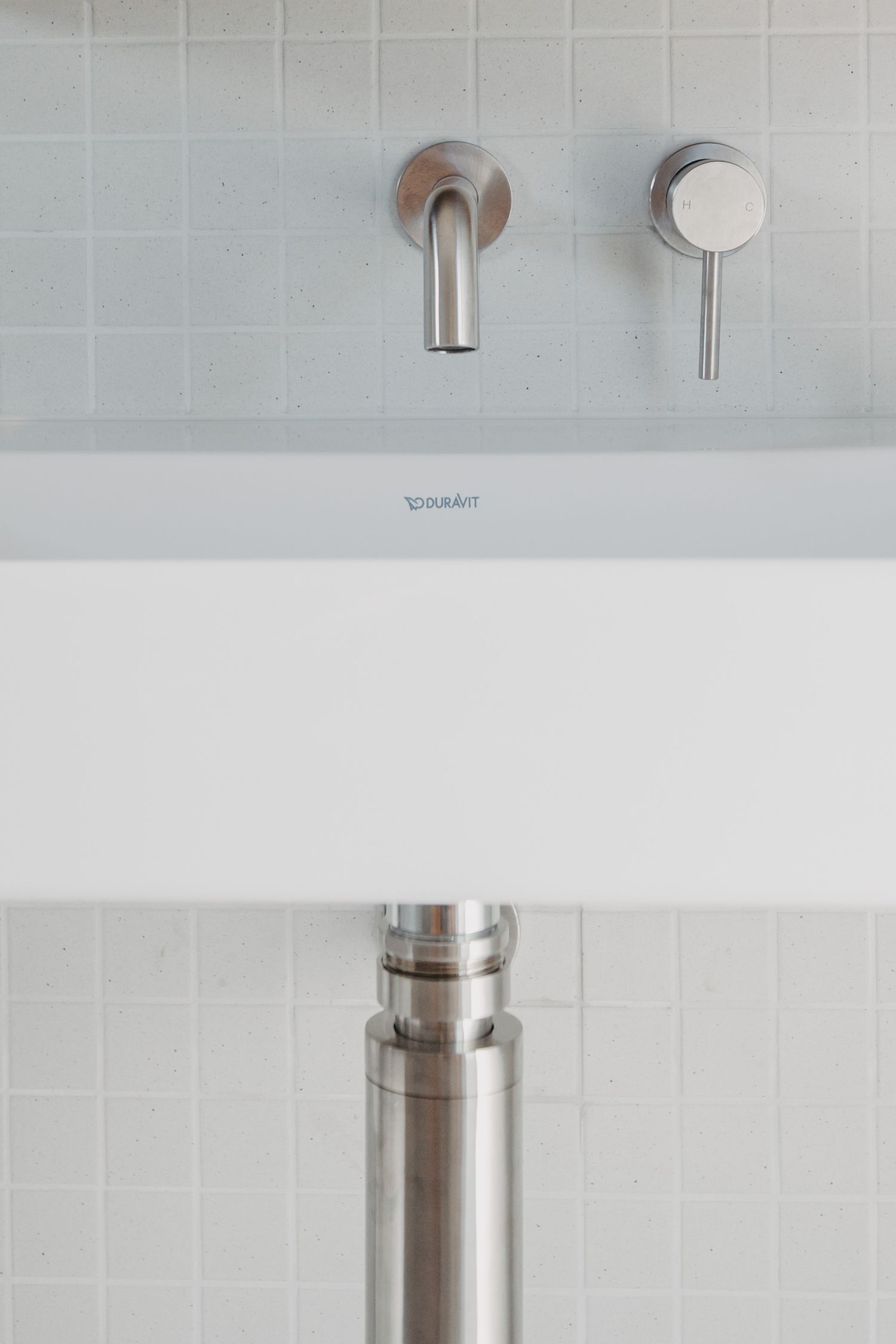 Close-up of Duravit wall-mounted sink with brushed chrome wall faucet and small square white mosaic tile backsplash.