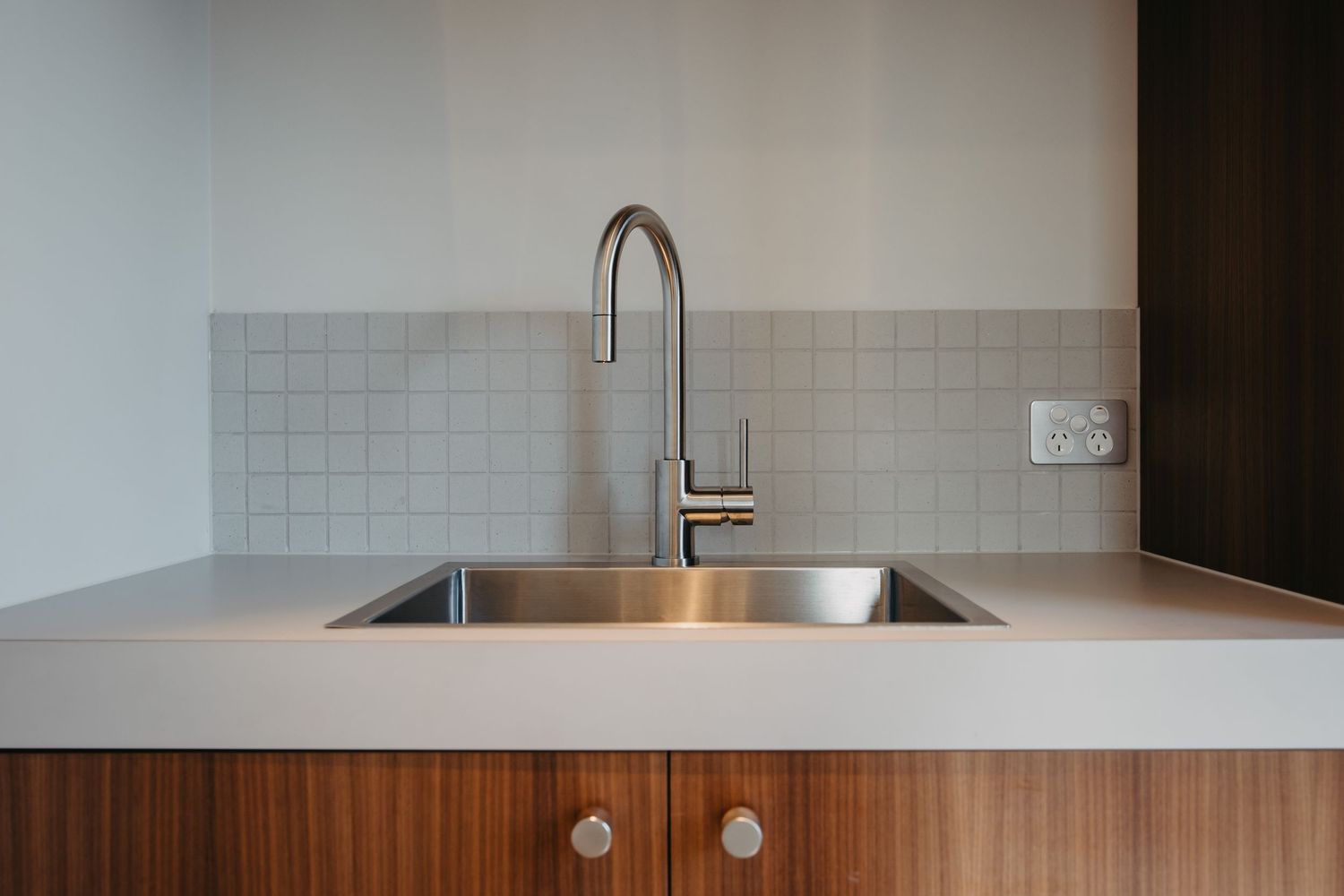 Modern kitchen detail with stainless steel double sink, brushed chrome gooseneck faucet, and walnut wood cabinetry.