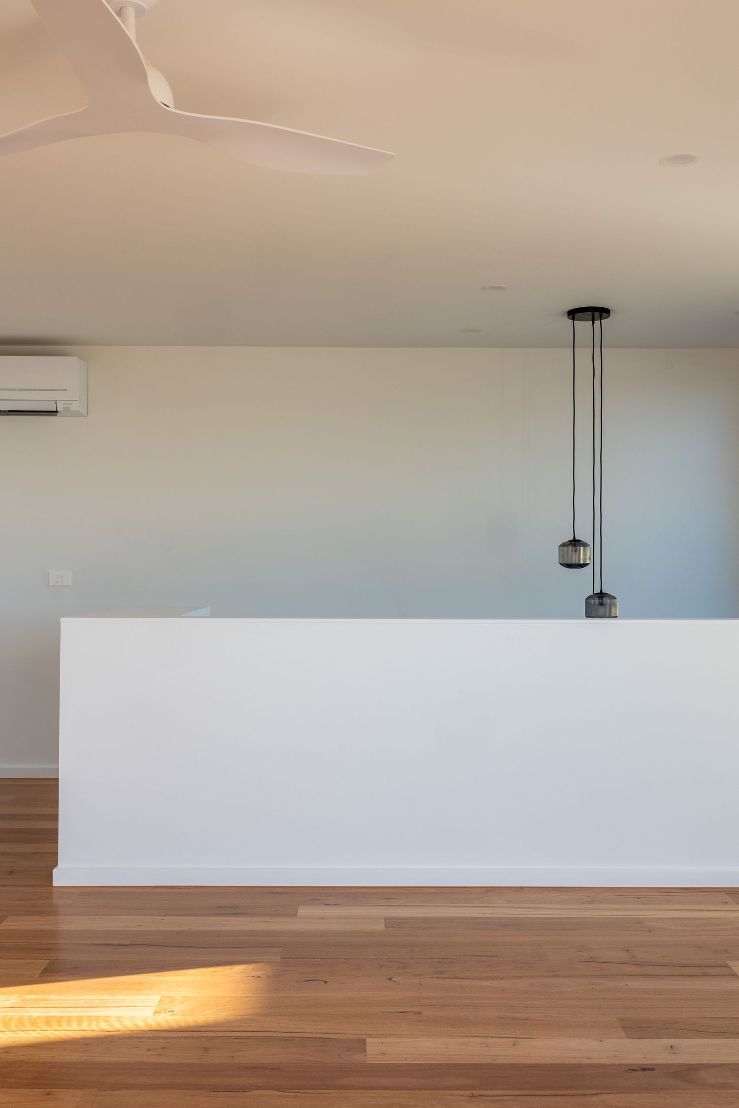 Modern minimalist kitchen island with hardwood floors, pendant lights, ceiling fan, and wall-mounted air conditioner.