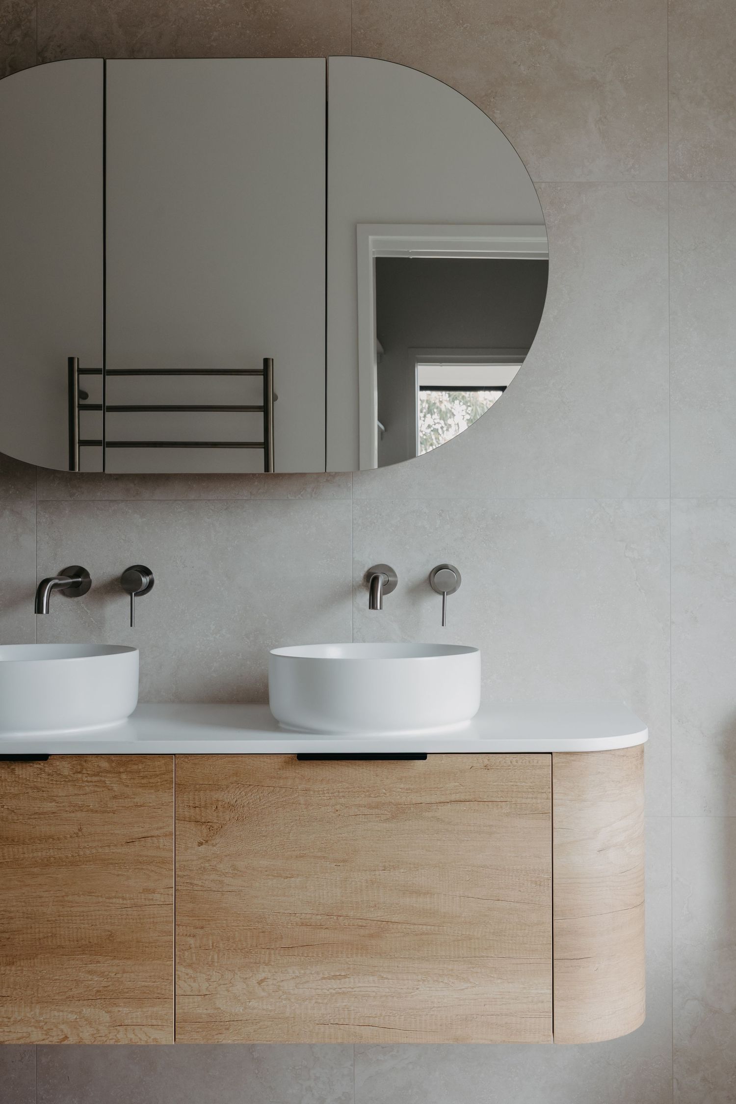 Floating timber double vanity with twin round vessel sinks, wall-mounted taps, and arched mirror cabinet.