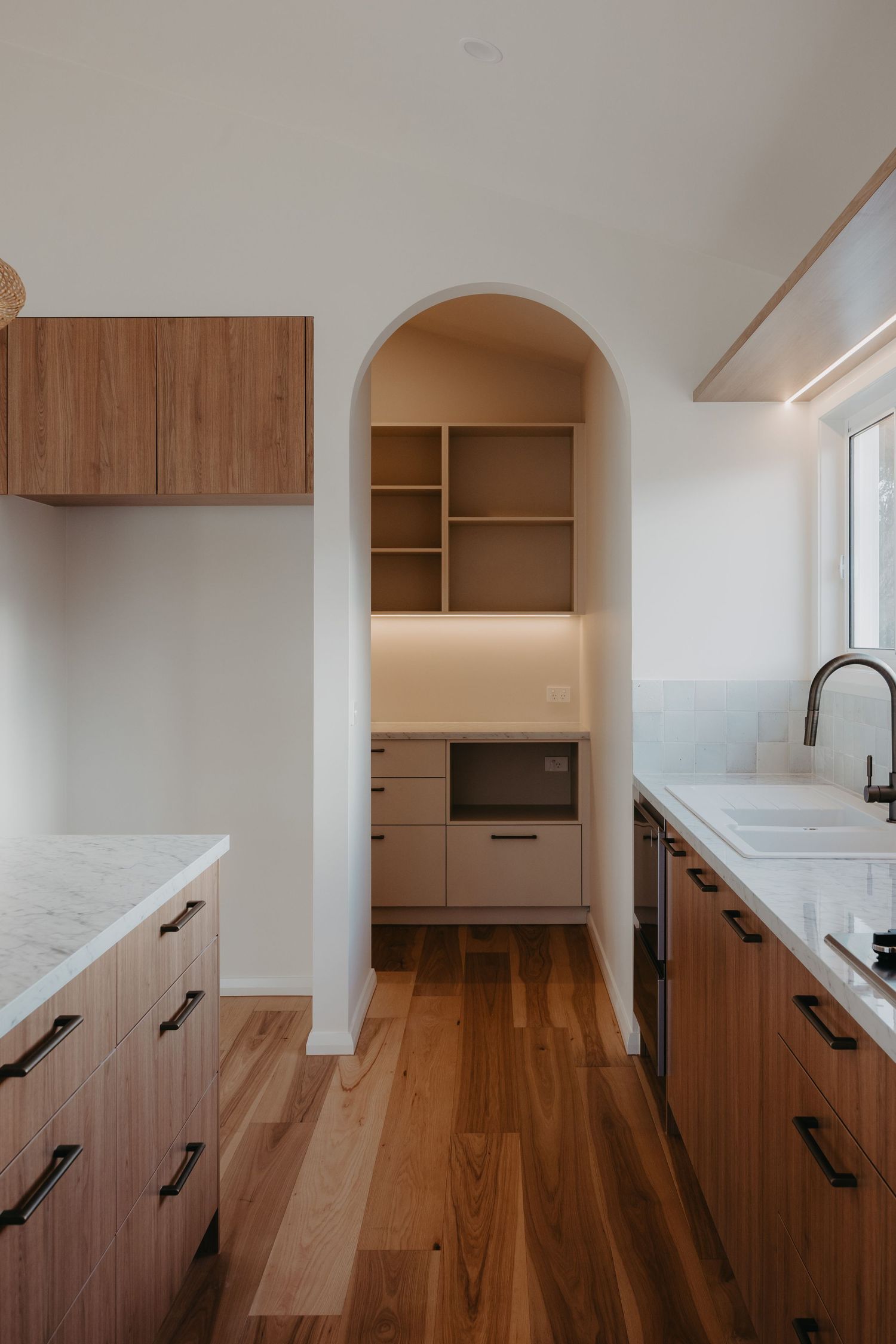 Stylish kitchen with timber drawers, arched pantry nook with open shelving, microwave cabinet, and warm hardwood flooring throughout.