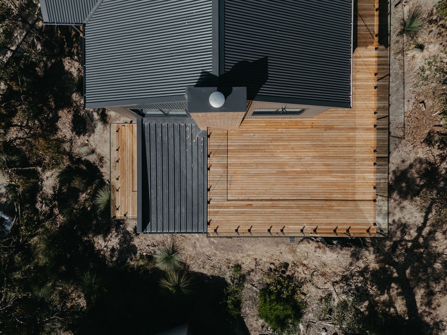 Aerial view of timber deck with outdoor furniture beside dark corrugated metal building.