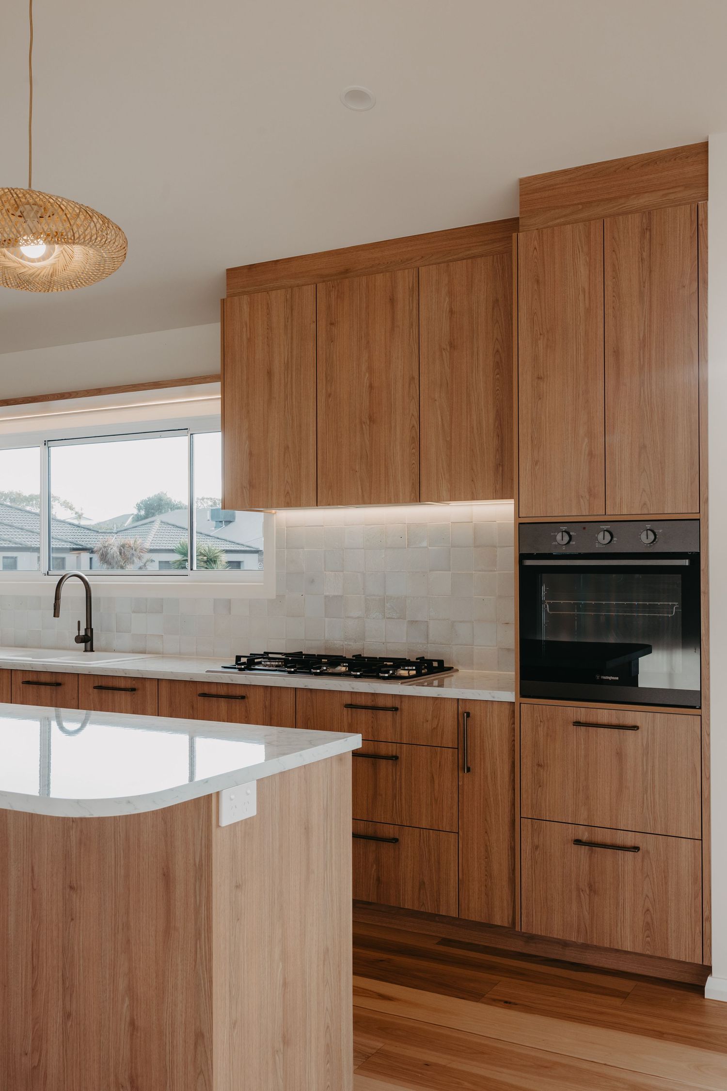 Modern kitchen featuring floor-to-ceiling timber cabinetry, black built-in oven, gas cooktop, marble benchtop, and subtle tile splashback.