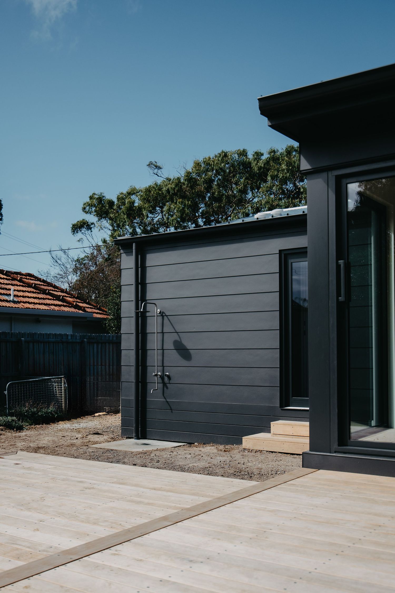 Dark charcoal cladded modern home exterior with outdoor shower, timber deck, and sliding glass door.