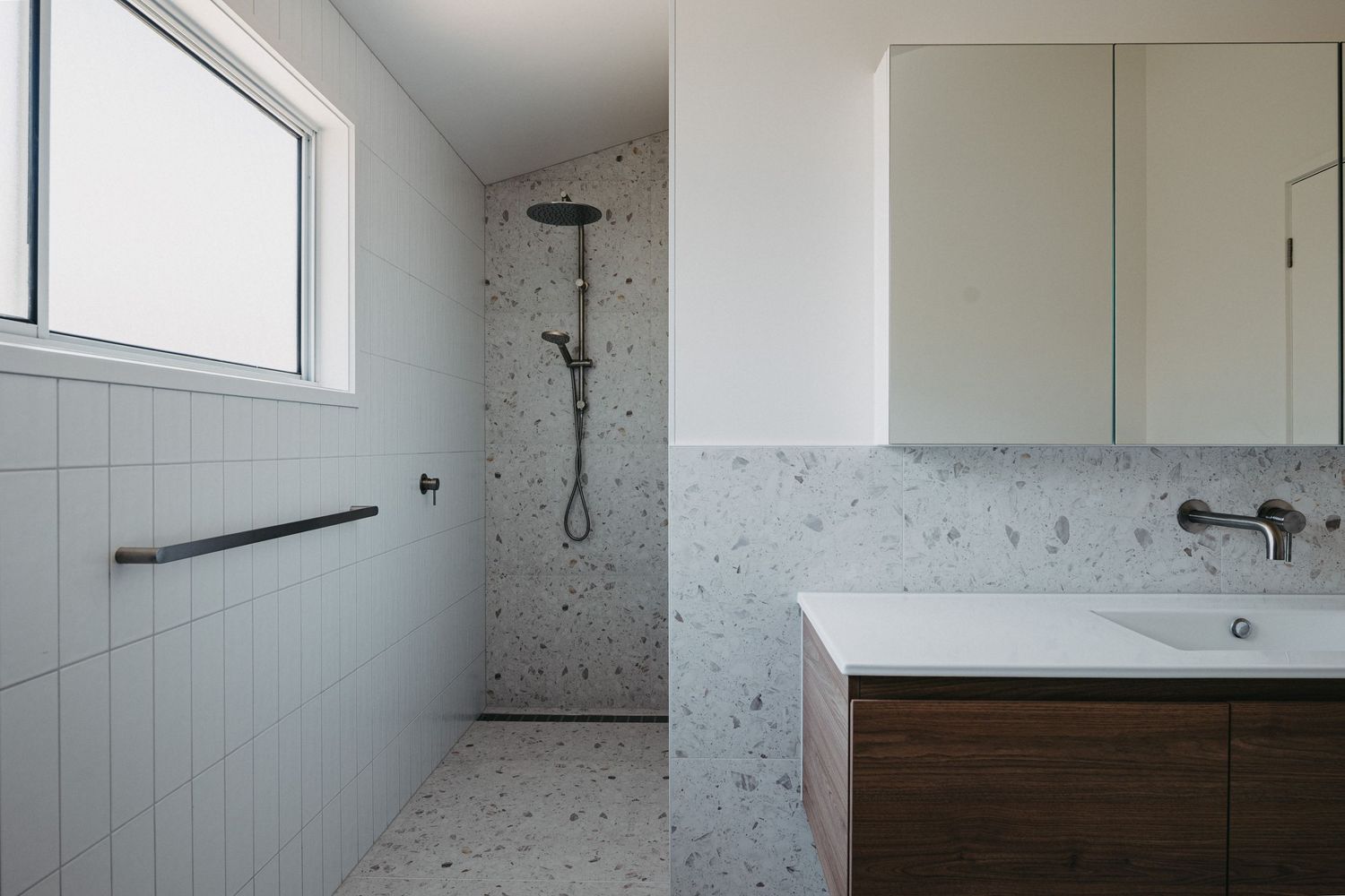 Modern bathroom with terrazzo tiles, walk-in shower, floating wood vanity, white subway tiles, and mirrored medicine cabinet.