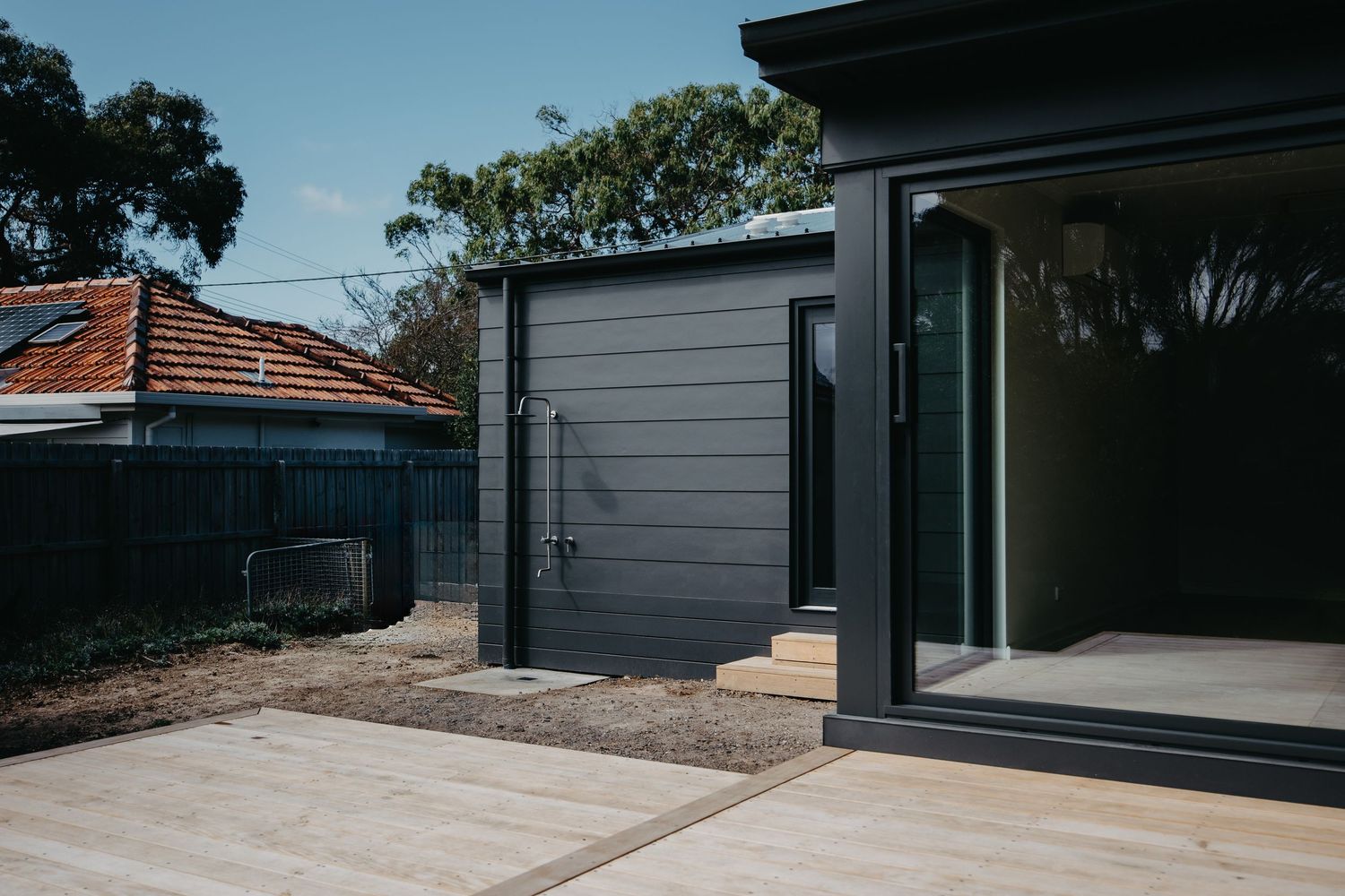 Modern dark charcoal exterior cladding with outdoor shower, timber decking, and large sliding glass door.