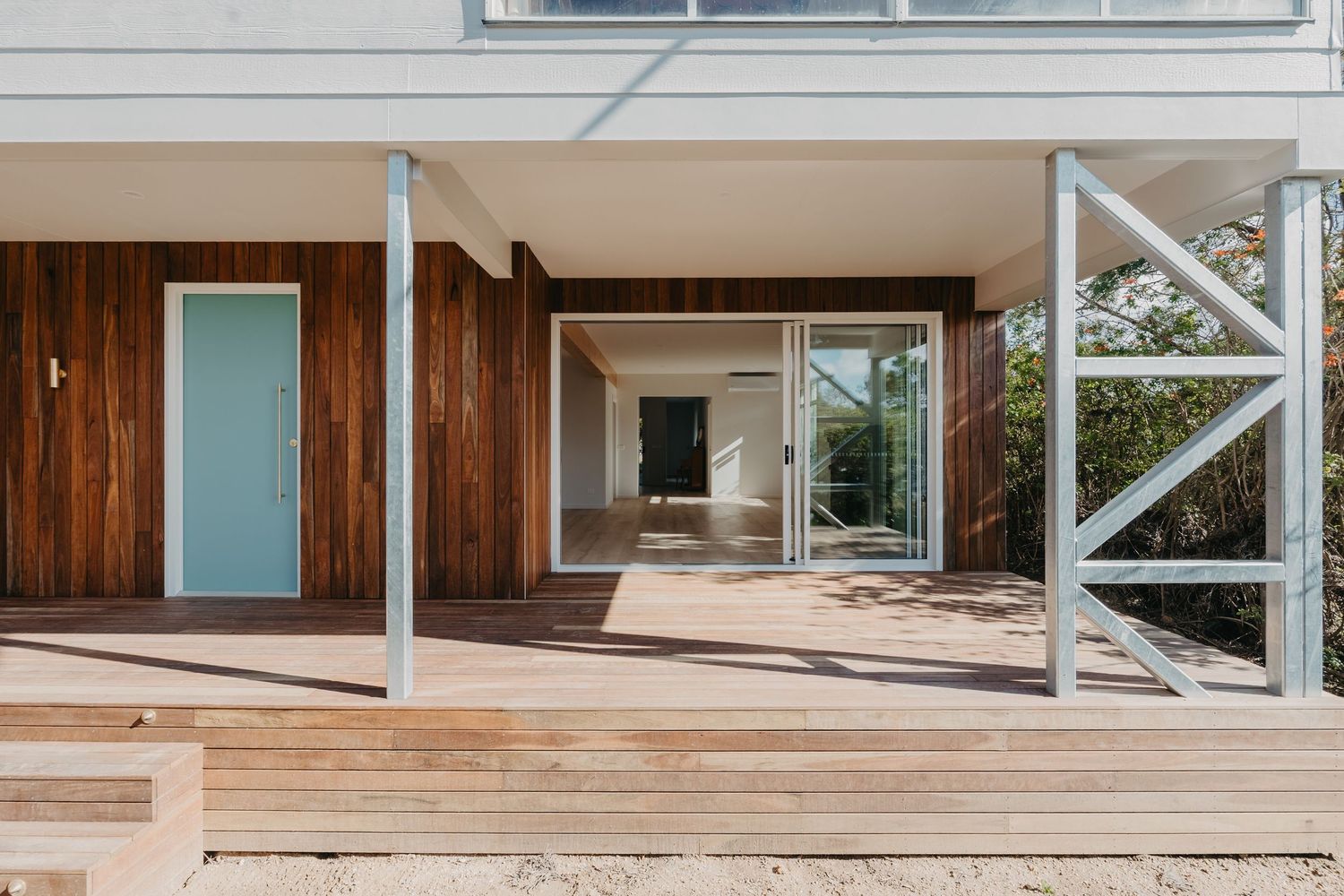 Timber deck with steel frame pergola, teak cladding, and light blue door on modern home exterior.
