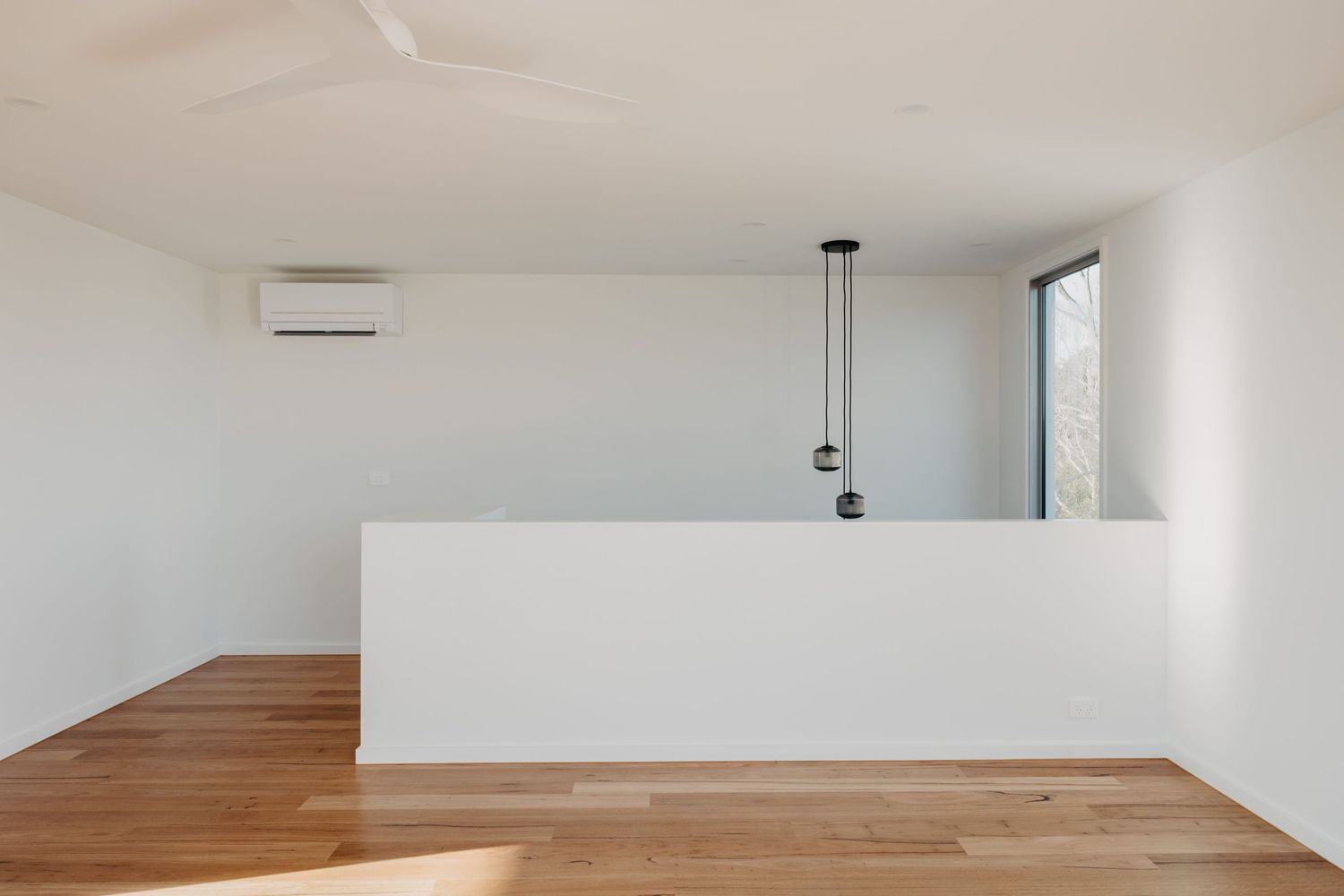 Minimalist white interior with timber floors, pendant lights, split system AC and stairwell divider wall.