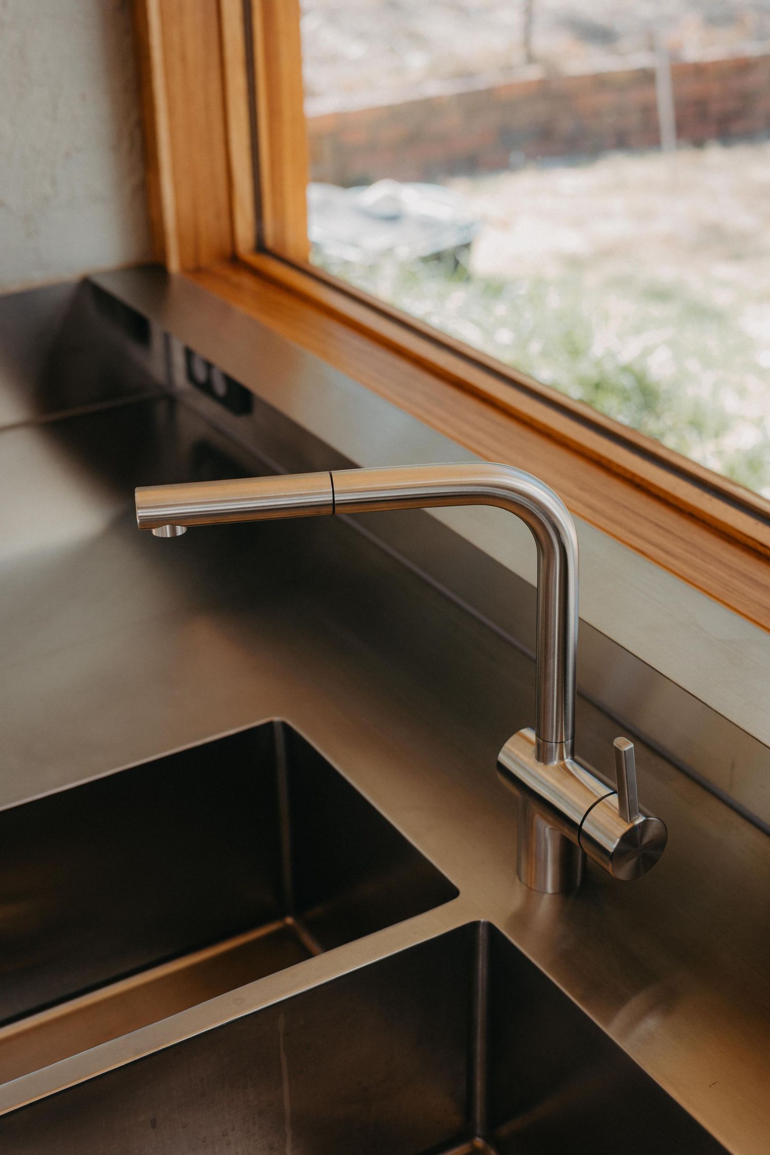 Stainless steel kitchen sink and modern pull-out faucet beside a timber-framed window.