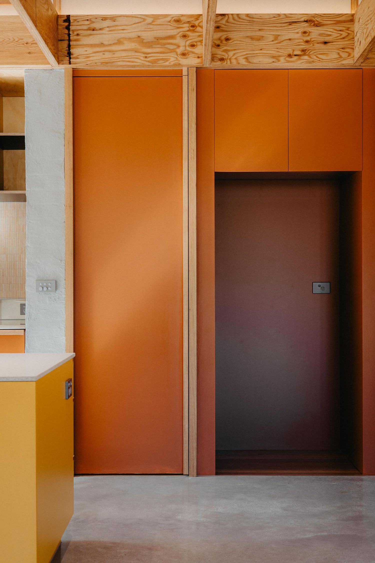 Bold orange and terracotta built-in cabinetry with plywood ceiling and polished concrete floor.