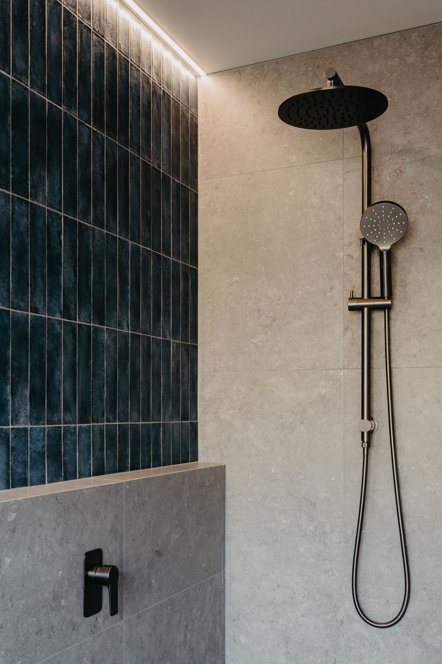 Luxury shower featuring dark teal vertical tiles, grey stone walls, matte black dual shower head, and LED strip lighting.