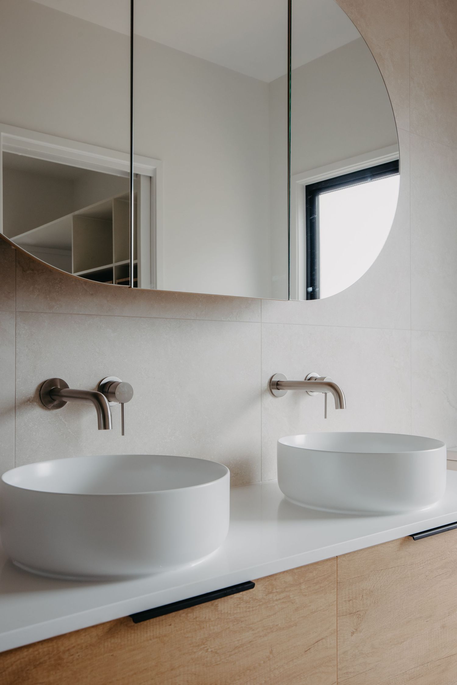 Double vessel sinks on timber vanity with brushed nickel wall-mounted tapware and arched medicine cabinet mirror.