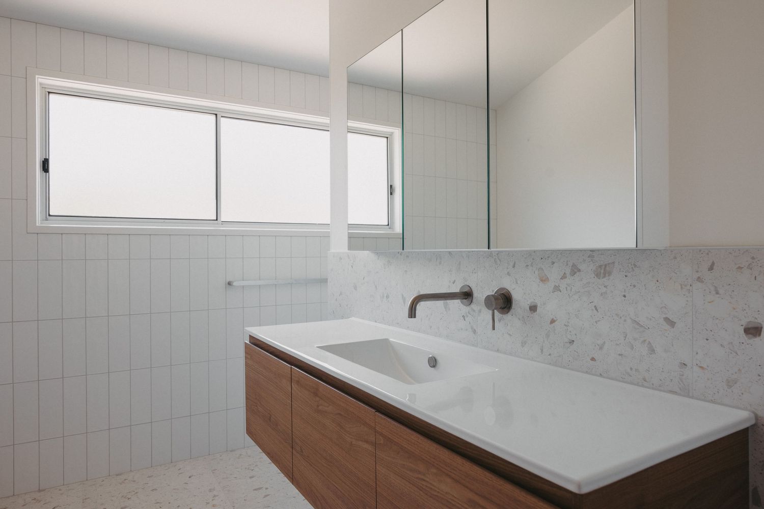 Modern bathroom vanity with walnut cabinet, white quartz countertop, wall-mounted faucet, marble backsplash, and mirrored medicine cabinet.