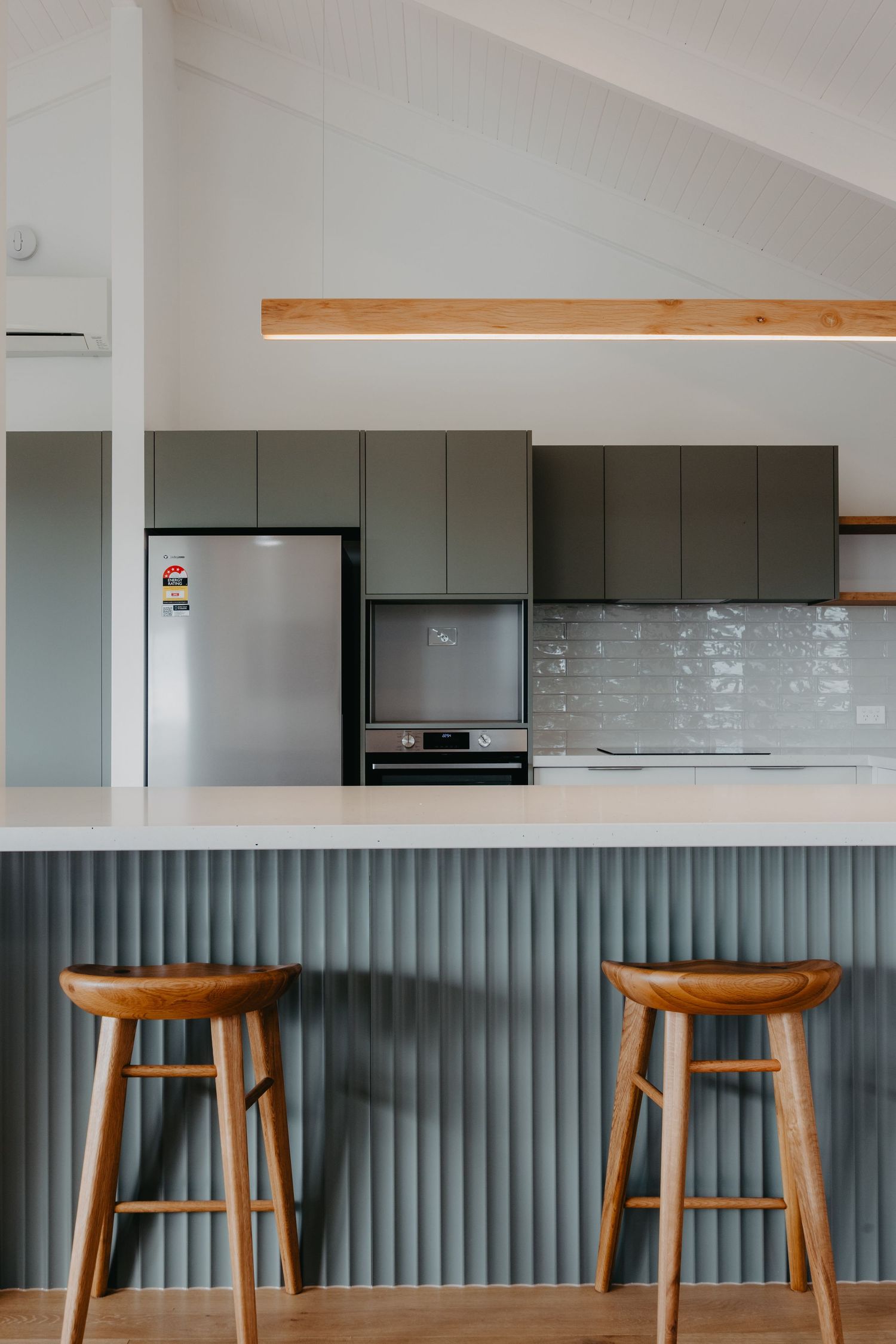 Contemporary kitchen featuring grey flat-panel cabinets, subway tile backsplash, and timber bar stools at island.