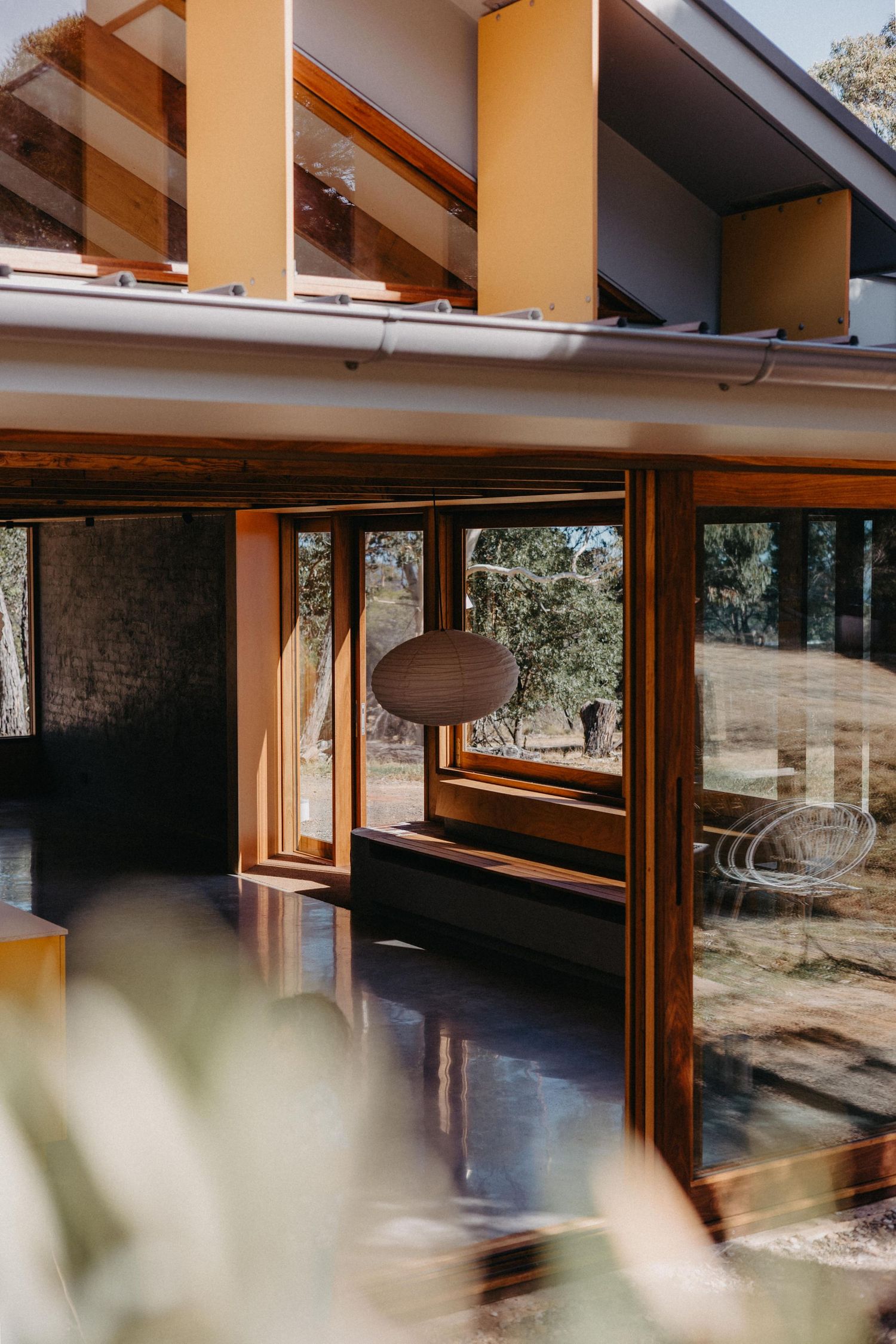 Mid-century modern home exterior featuring warm timber frames, large glass windows, and a paper lantern pendant light.