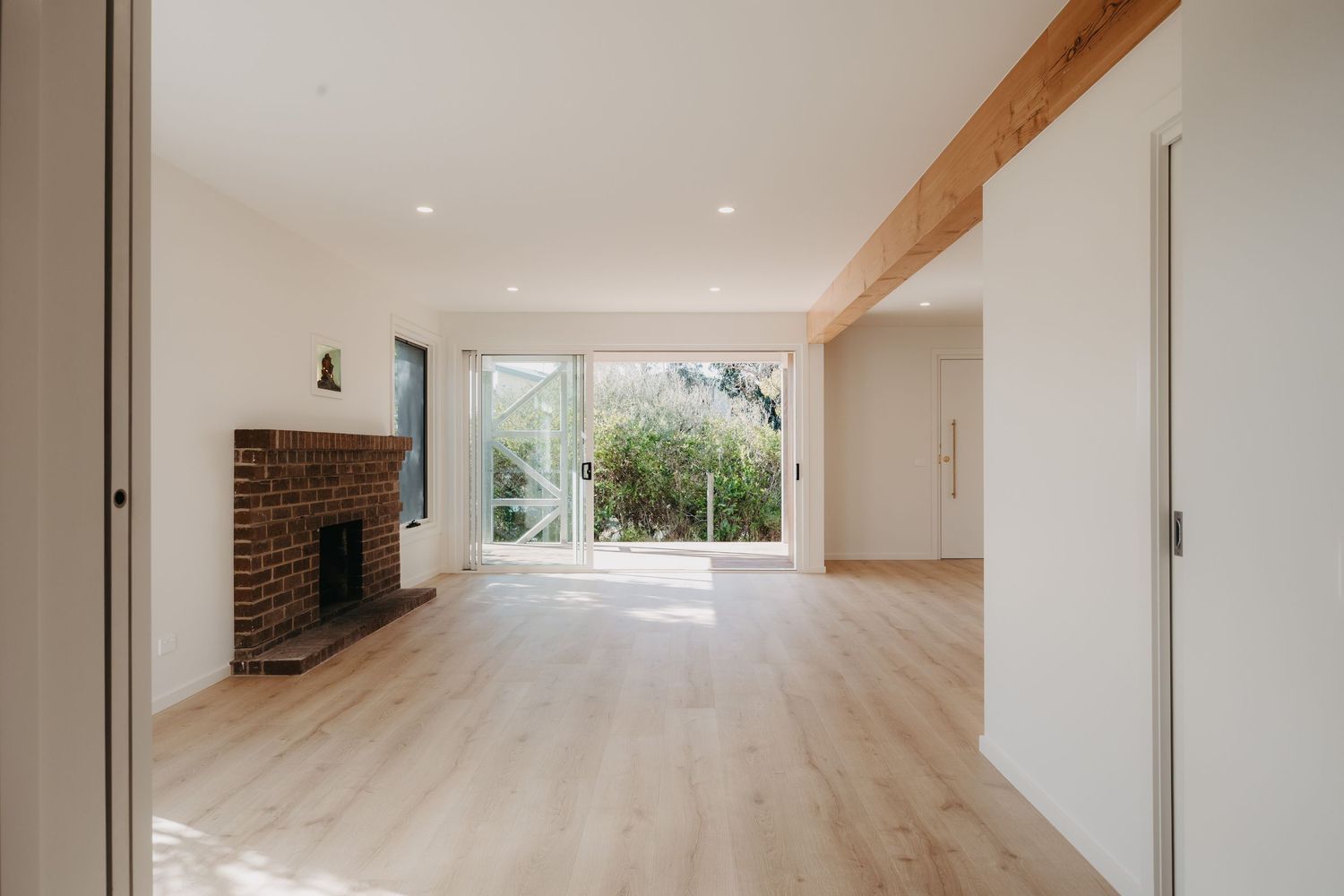 Bright open living room with exposed timber beam, brick fireplace, and sliding glass doors.
