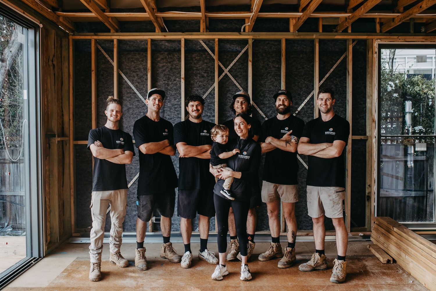 Group of seven construction workers in black uniforms posing inside a timber-framed building under renovation.