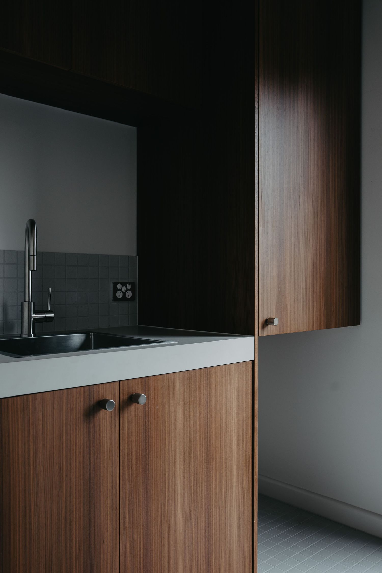 Modern kitchen with walnut cabinets, black sink, chrome faucet, and dark tile backsplash.