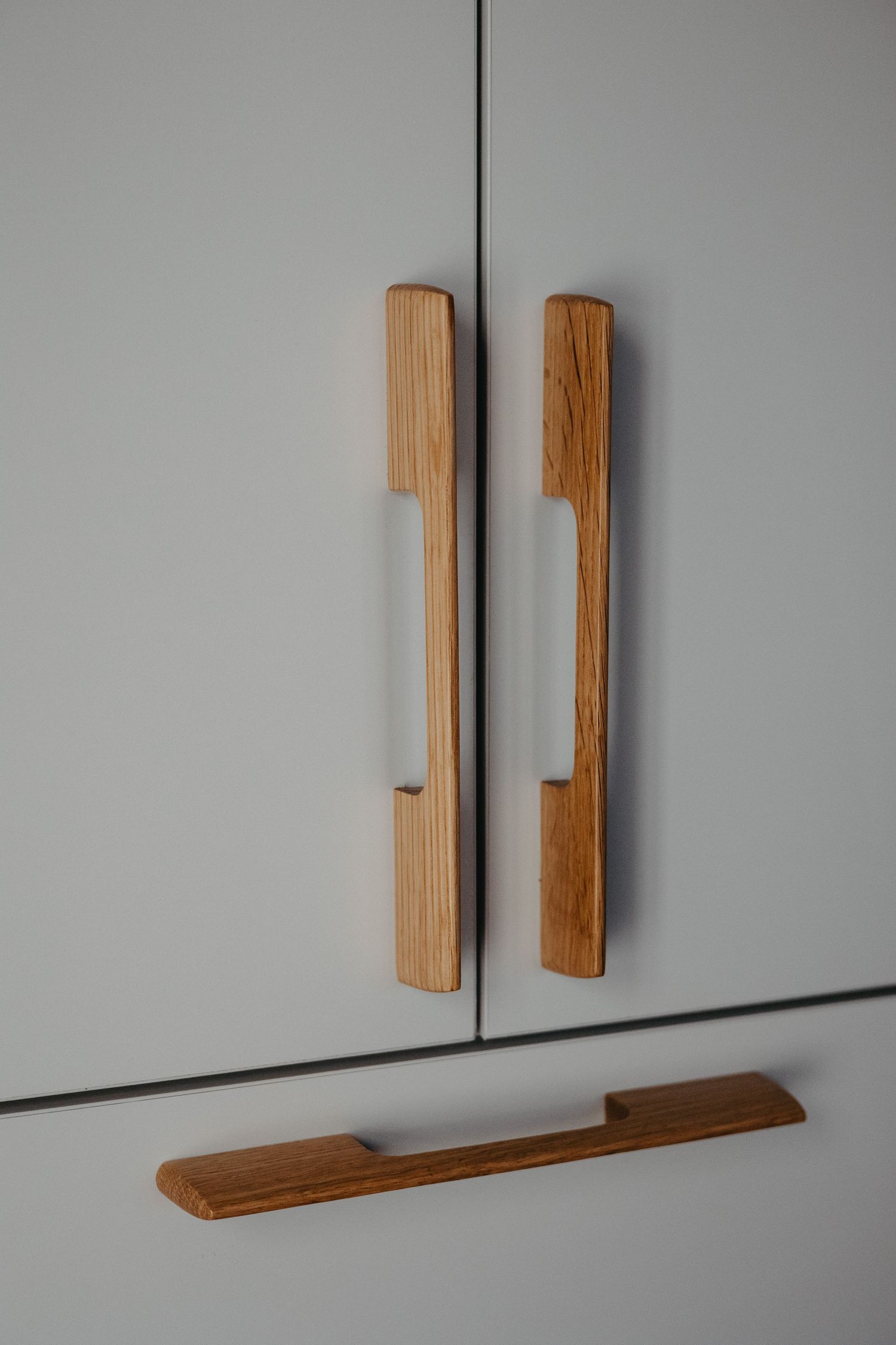 Close-up of two wooden cabinet handles on gray doors with a matching drawer pull below.
