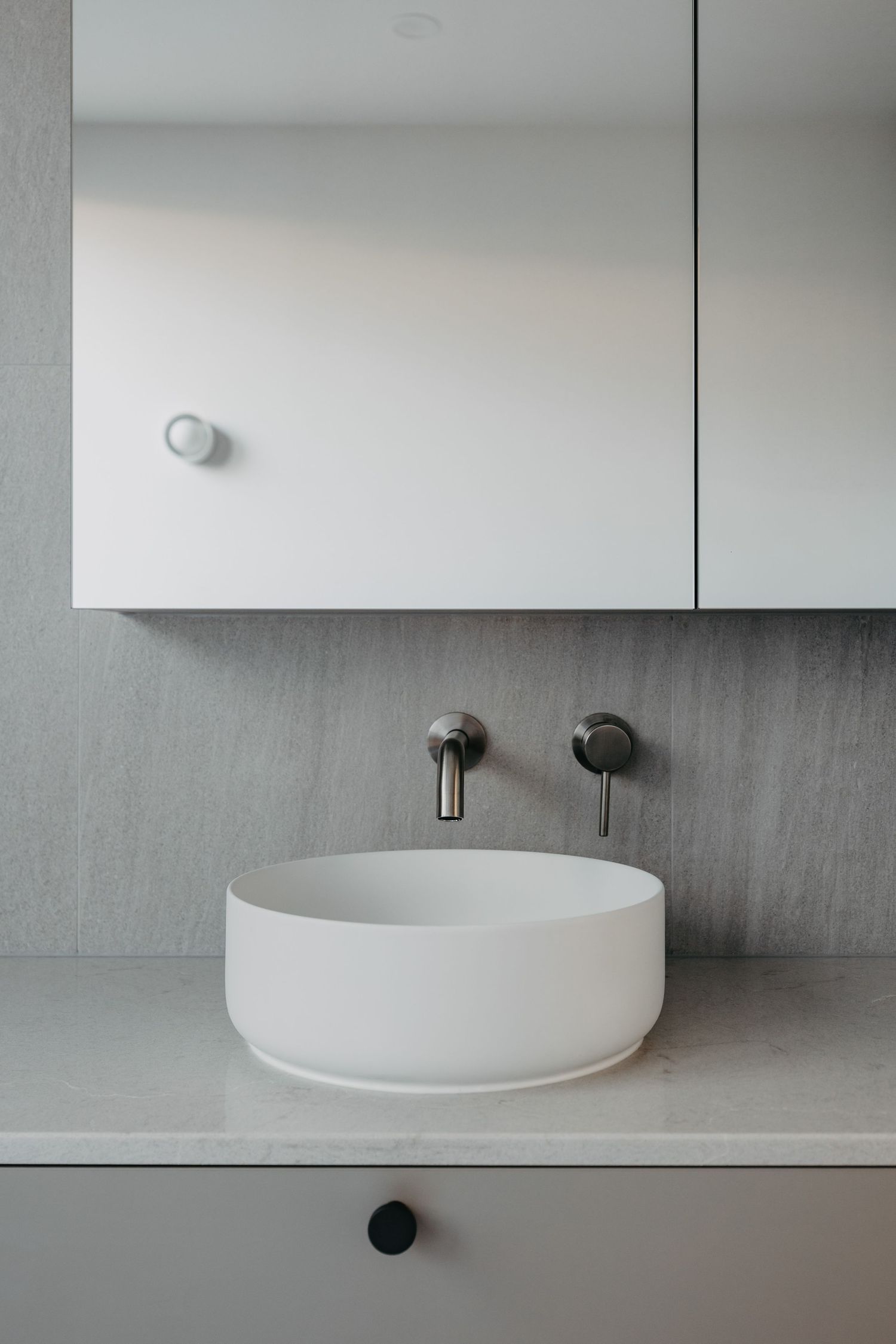 Modern bathroom with white vessel sink, wall-mounted chrome faucet, marble countertop, and mirrored medicine cabinet.