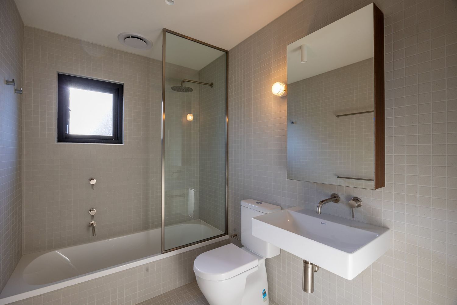 Modern bathroom with glass shower, soaking tub, white floating sink, toilet, and mirror cabinet with neutral tile walls.