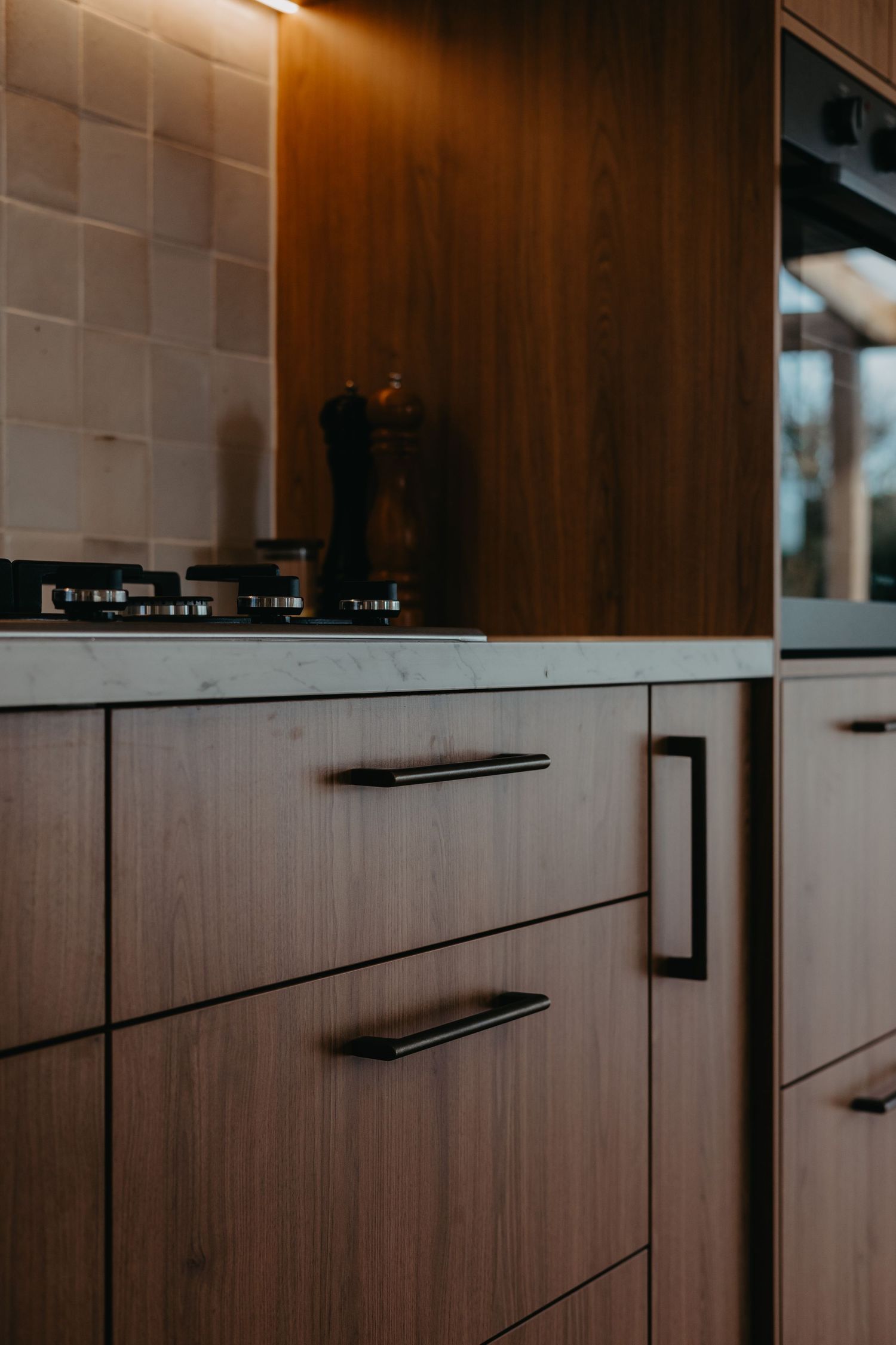 Modern kitchen cabinetry featuring warm wood grain drawers with sleek black handles and tile backsplash.
