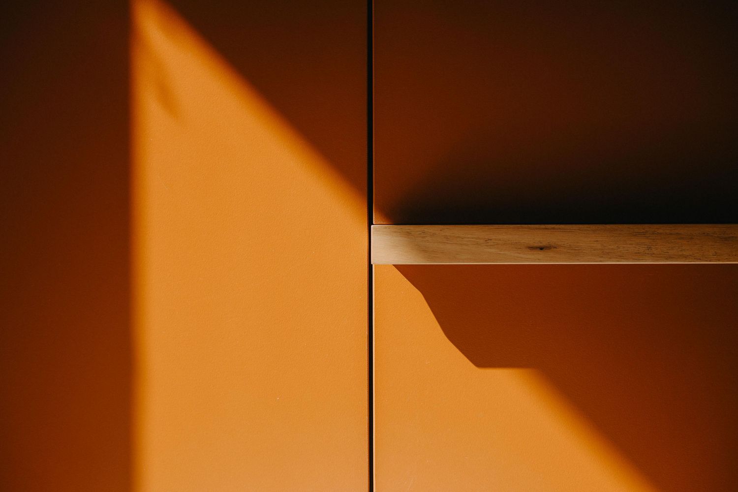 Detail shot of orange cabinet doors with timber shelf edge and warm shadow play.