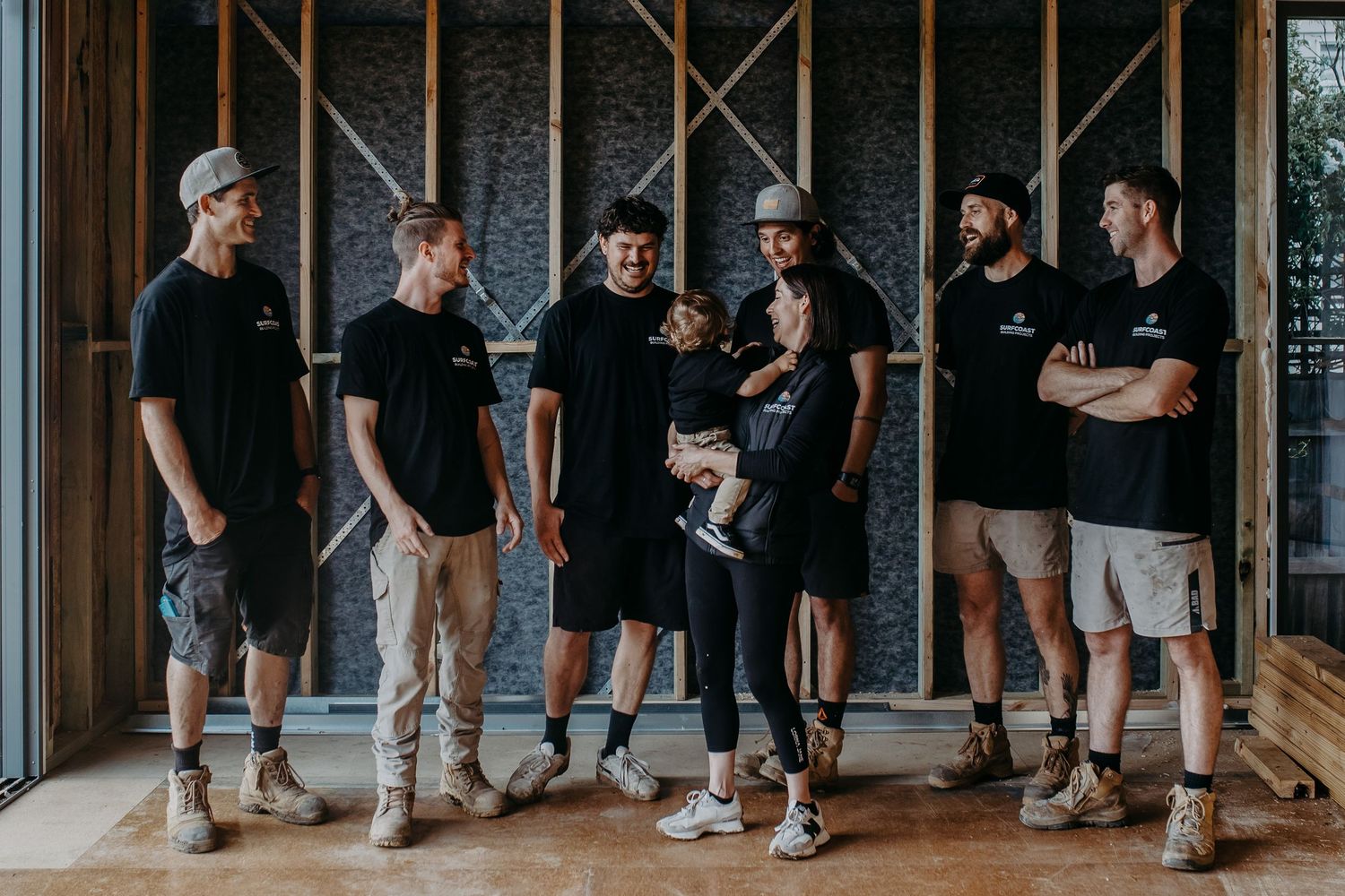 A group of seven construction workers in black shirts posing together inside an unfinished building.