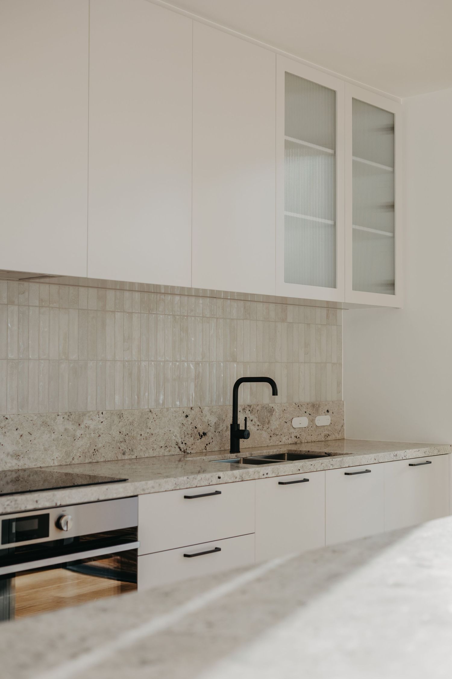 Modern white kitchen with granite countertops, black faucet, subway tile backsplash, and glass-front upper cabinets.