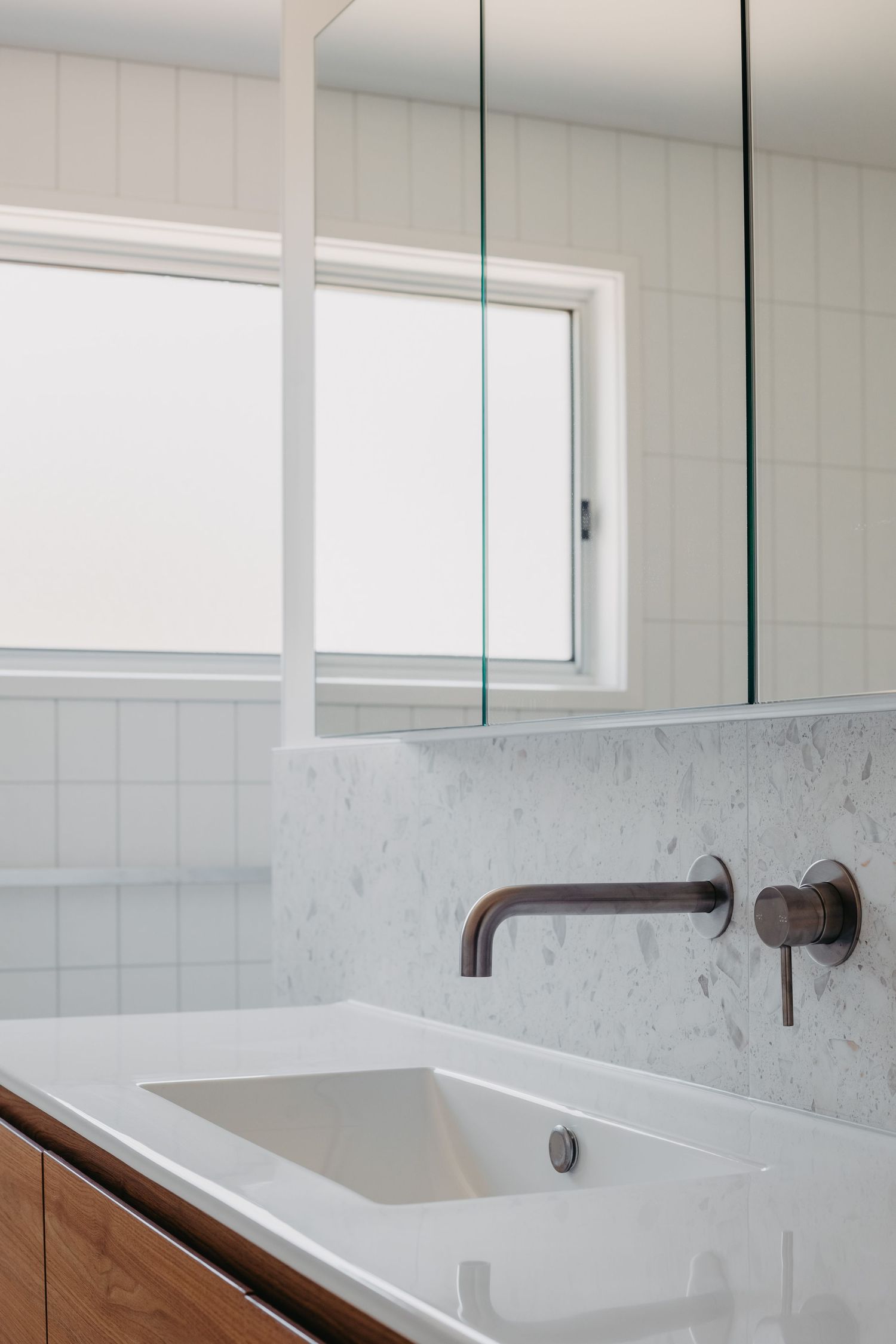Modern bathroom vanity with marble backsplash, bronze wall-mount faucet, white undermount sink, and mirrored medicine cabinet.
