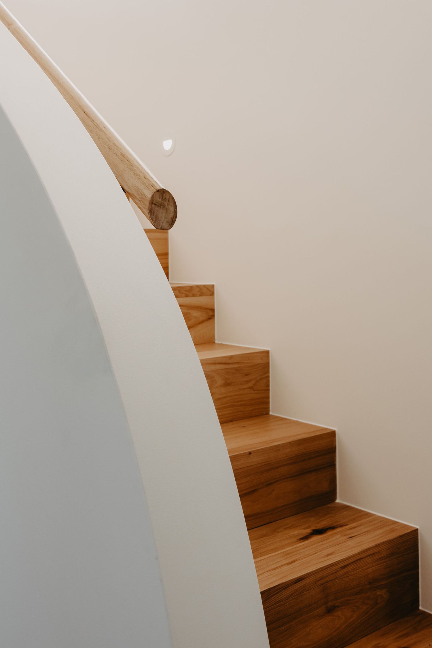 Elegant timber staircase with warm oak treads, curved white wall, and a rounded wooden handrail in a modern home.