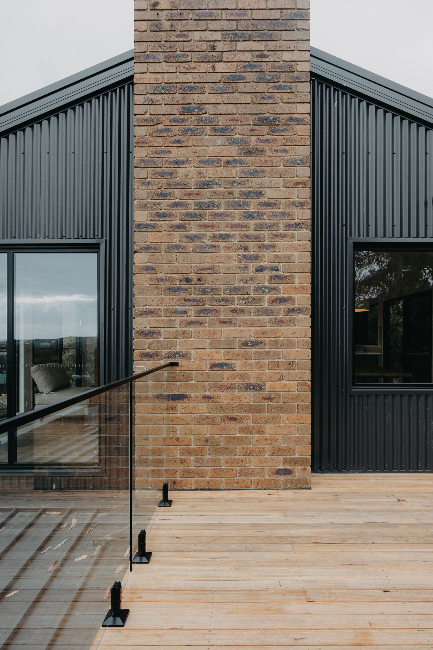 Modern home exterior featuring brick chimney, black corrugated cladding, and timber deck.