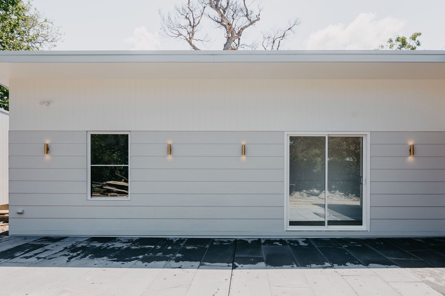 Modern white ranch-style home exterior with sliding glass door, wall sconces, and horizontal siding.