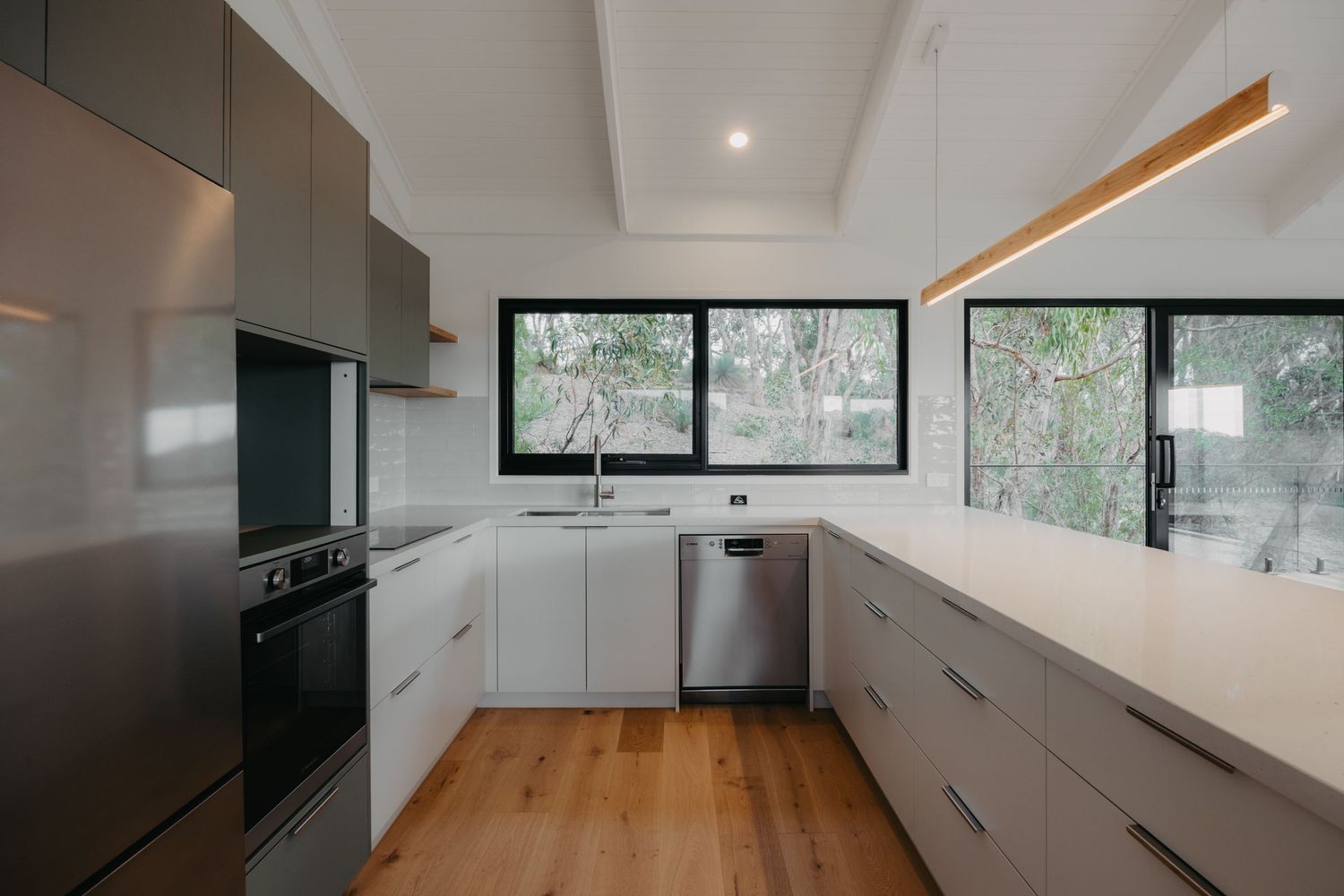 Sleek U-shaped kitchen with white benchtops, grey cabinetry, stainless steel appliances, and timber flooring.