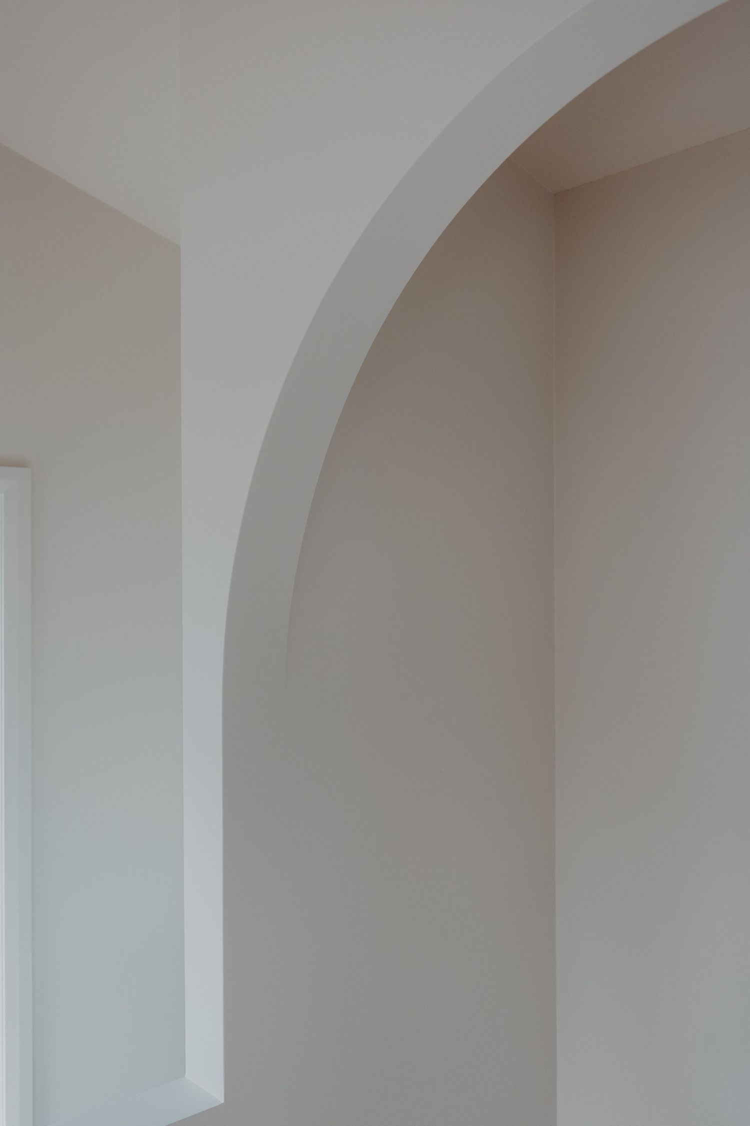 Elegant white interior arch with soft curves, neutral walls, and natural light creating a minimalist architectural detail.