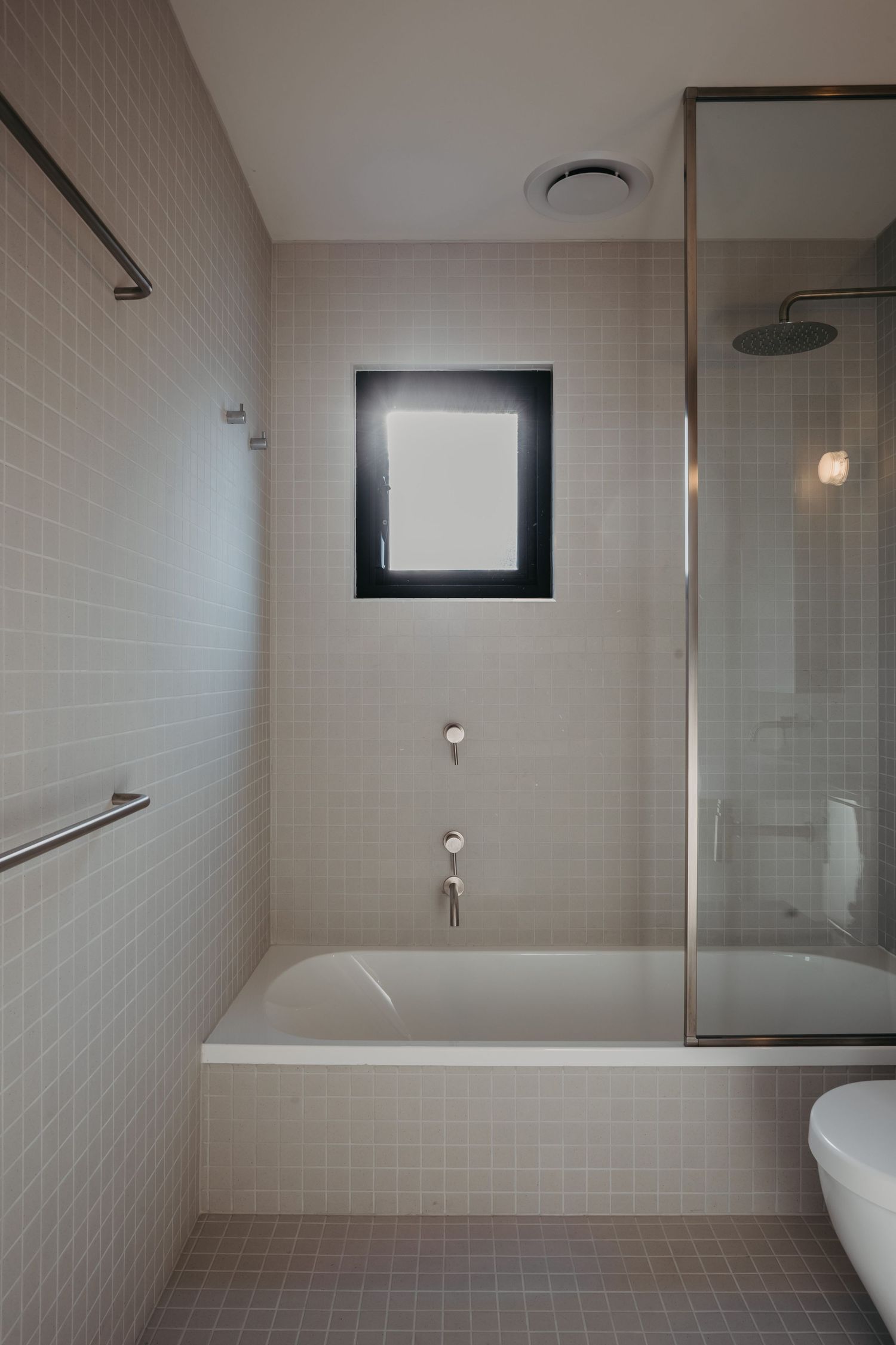 Clean modern bathroom with white subway tiles, soaking tub, small black-framed window, and glass shower enclosure.