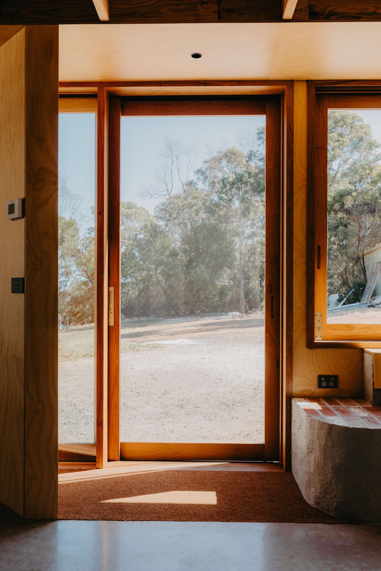 Open timber-framed door revealing a sunlit bushland landscape with eucalyptus trees beyond.