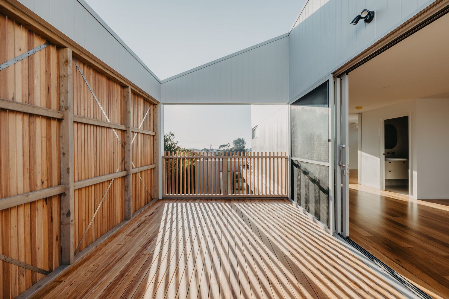 Timber decked balcony with wooden slat privacy wall and glass sliding doors opening to interior living space.
