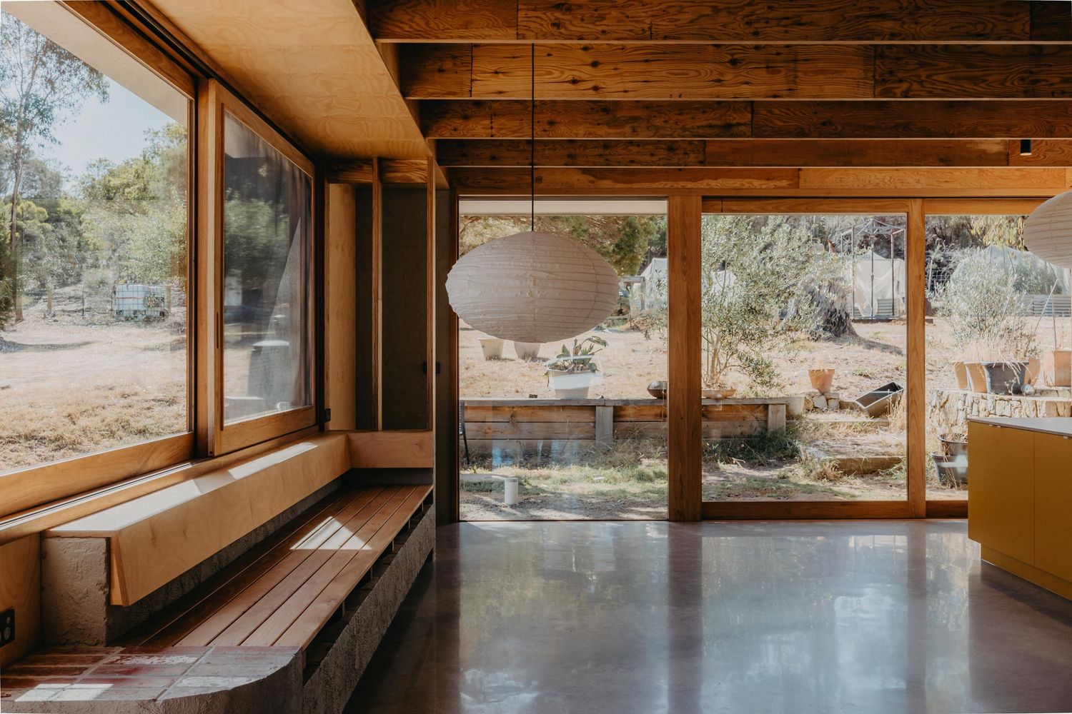Timber-lined interior with built-in bench seat, polished concrete floor, and sliding doors to garden.